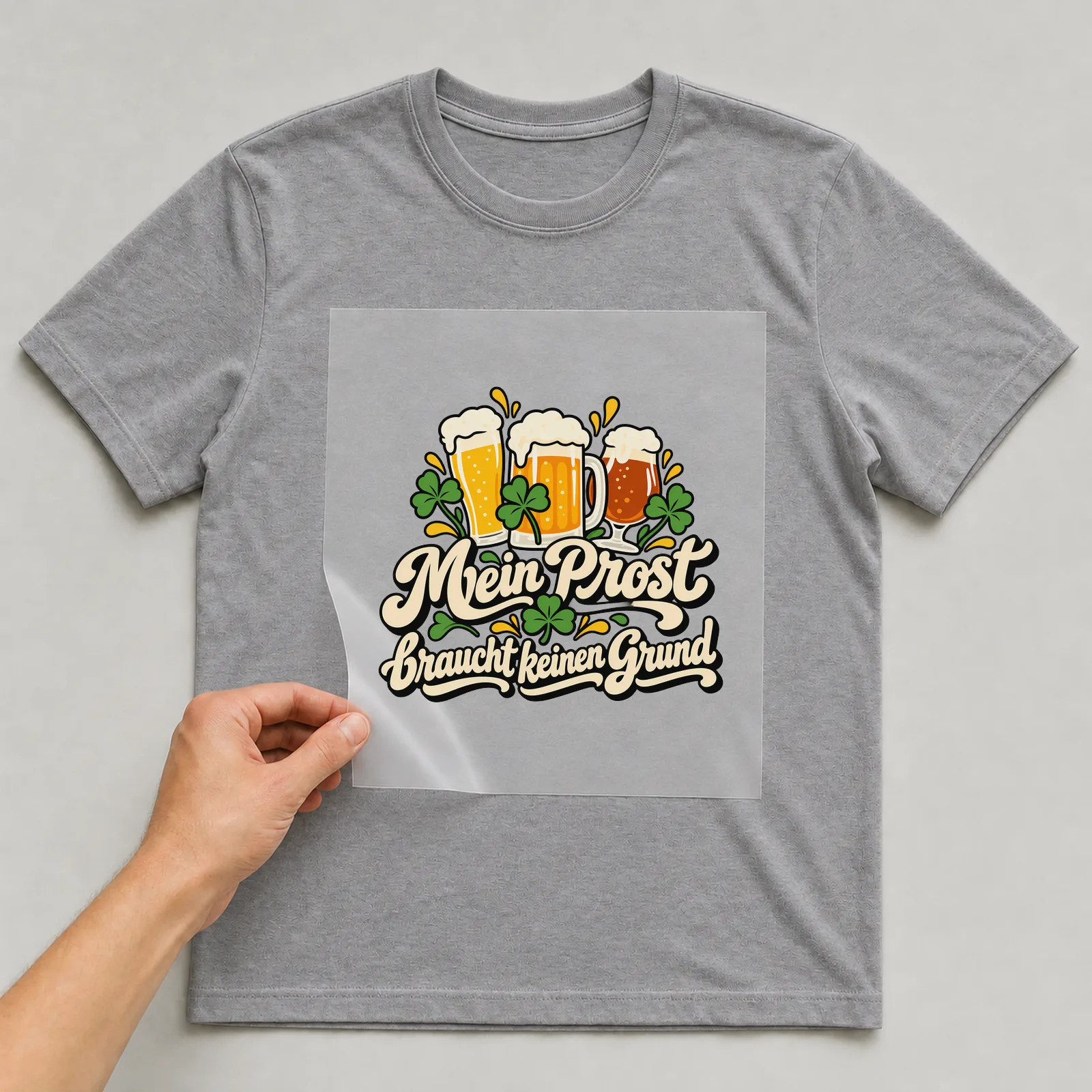 Bügelbild „Mein Prost braucht keinen Grund“ auf grauem T-Shirt, Folie wird aufgelegt