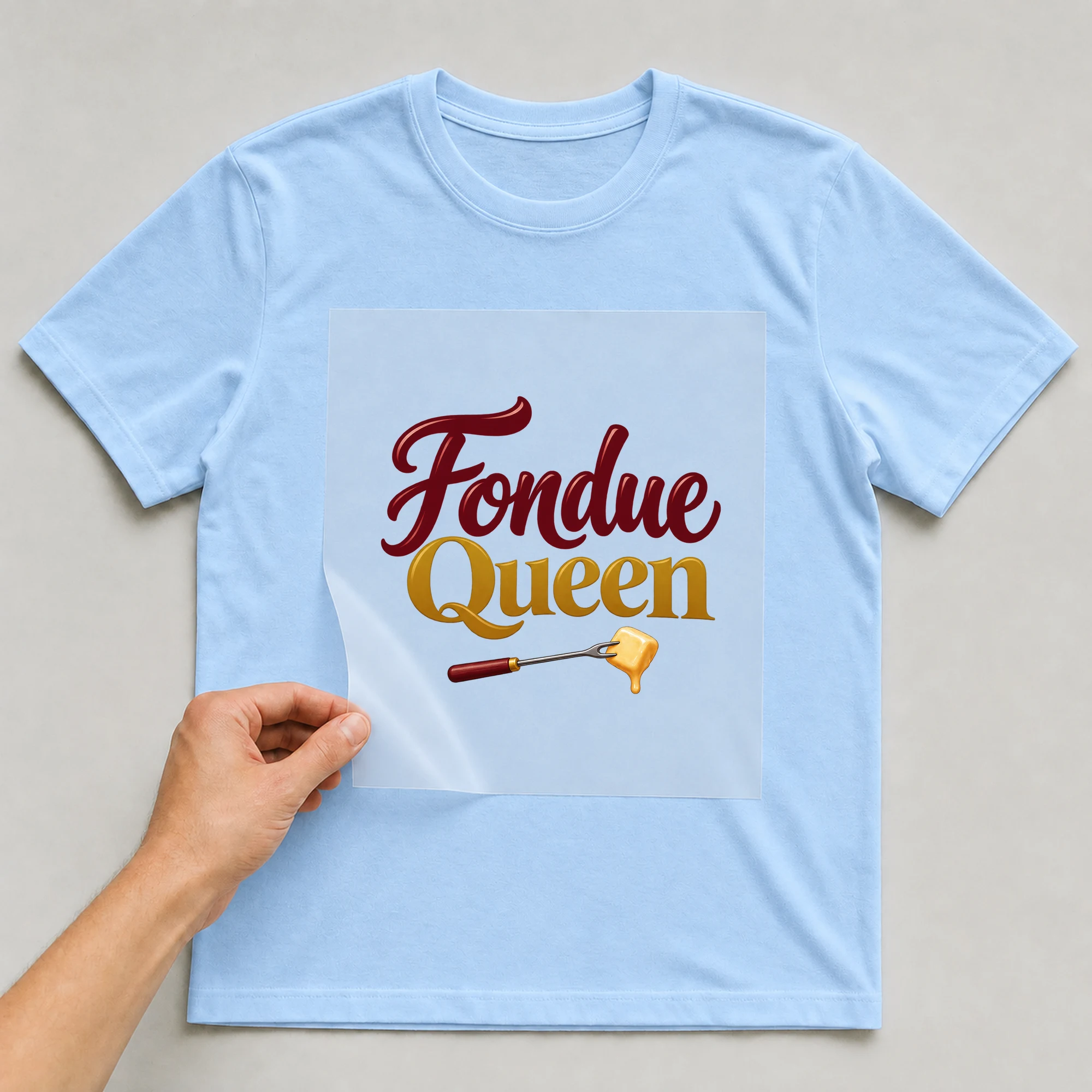 Bügelbild „Fondue Queen“ auf babyblauem T-Shirt, Folie wird aufgelegt