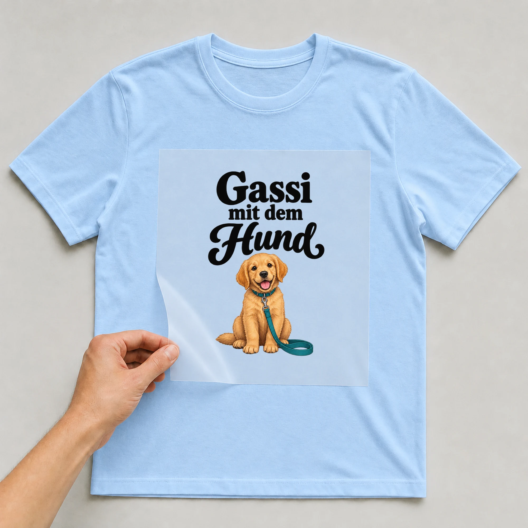 Bügelbild „Gassi mit dem Hund“ auf babyblauem T-Shirt, Folie wird aufgelegt