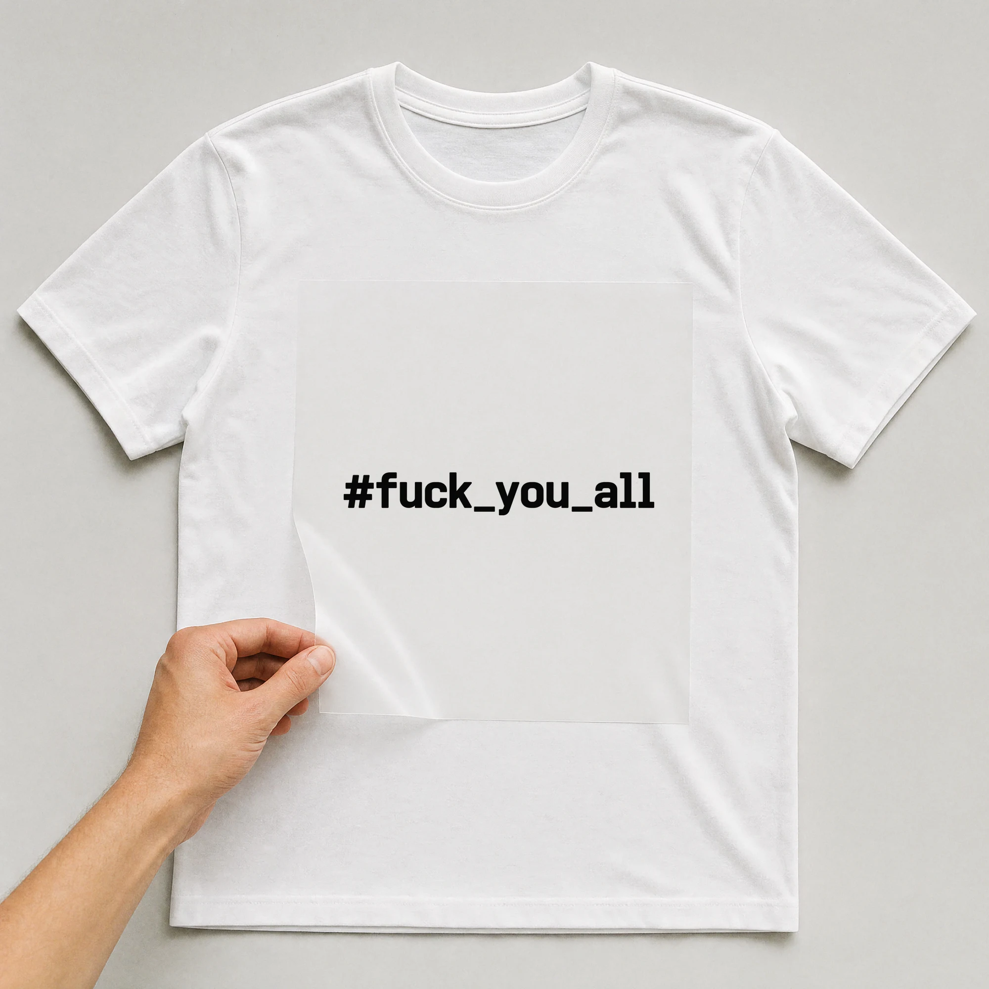 Bügelbild „#f*ck_you_all“ auf weißem T-Shirt, Folie wird aufgelegt