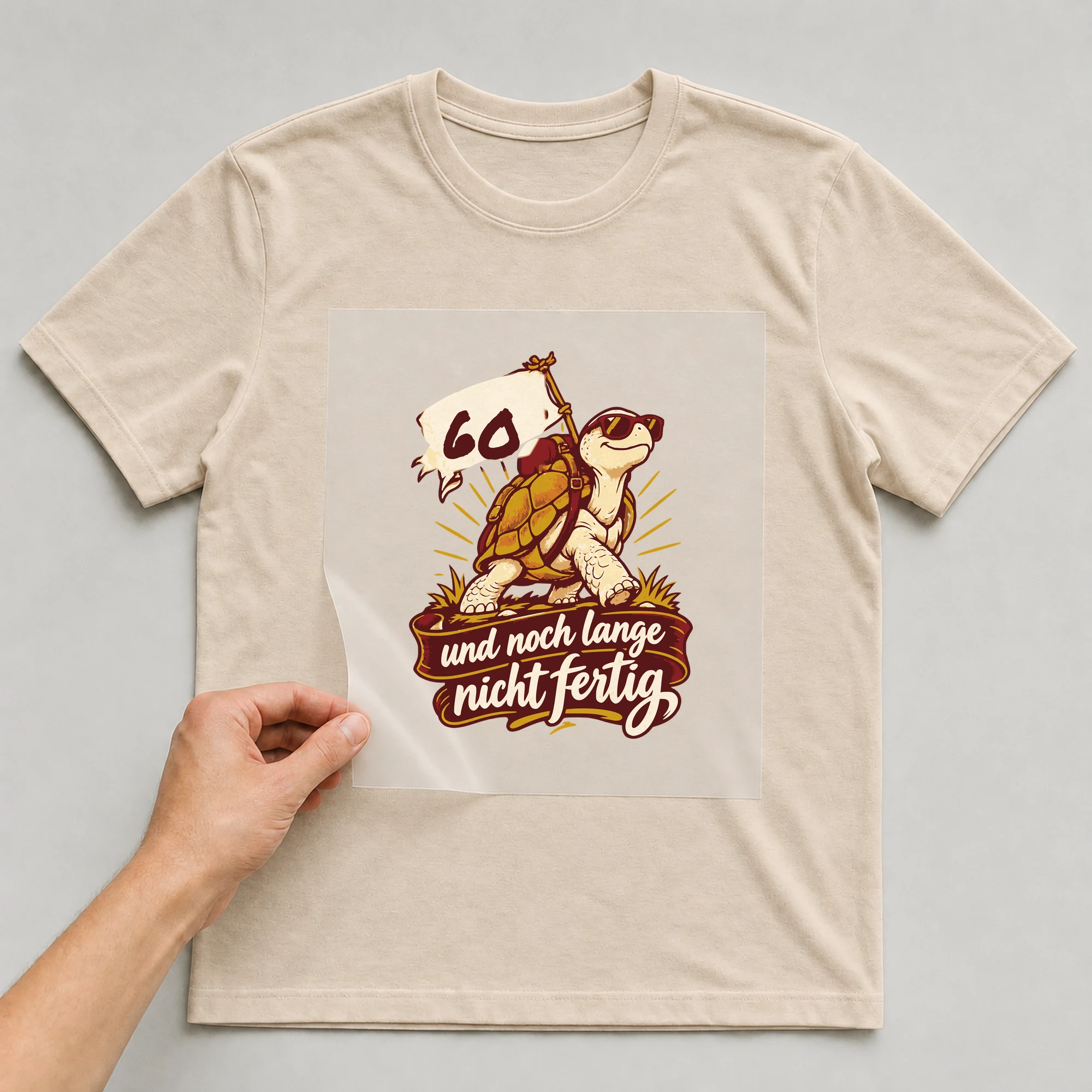 Bügelbild Und noch lange nicht fertig mit Alter auf beigem T-Shirt, Folie wird aufgelegt