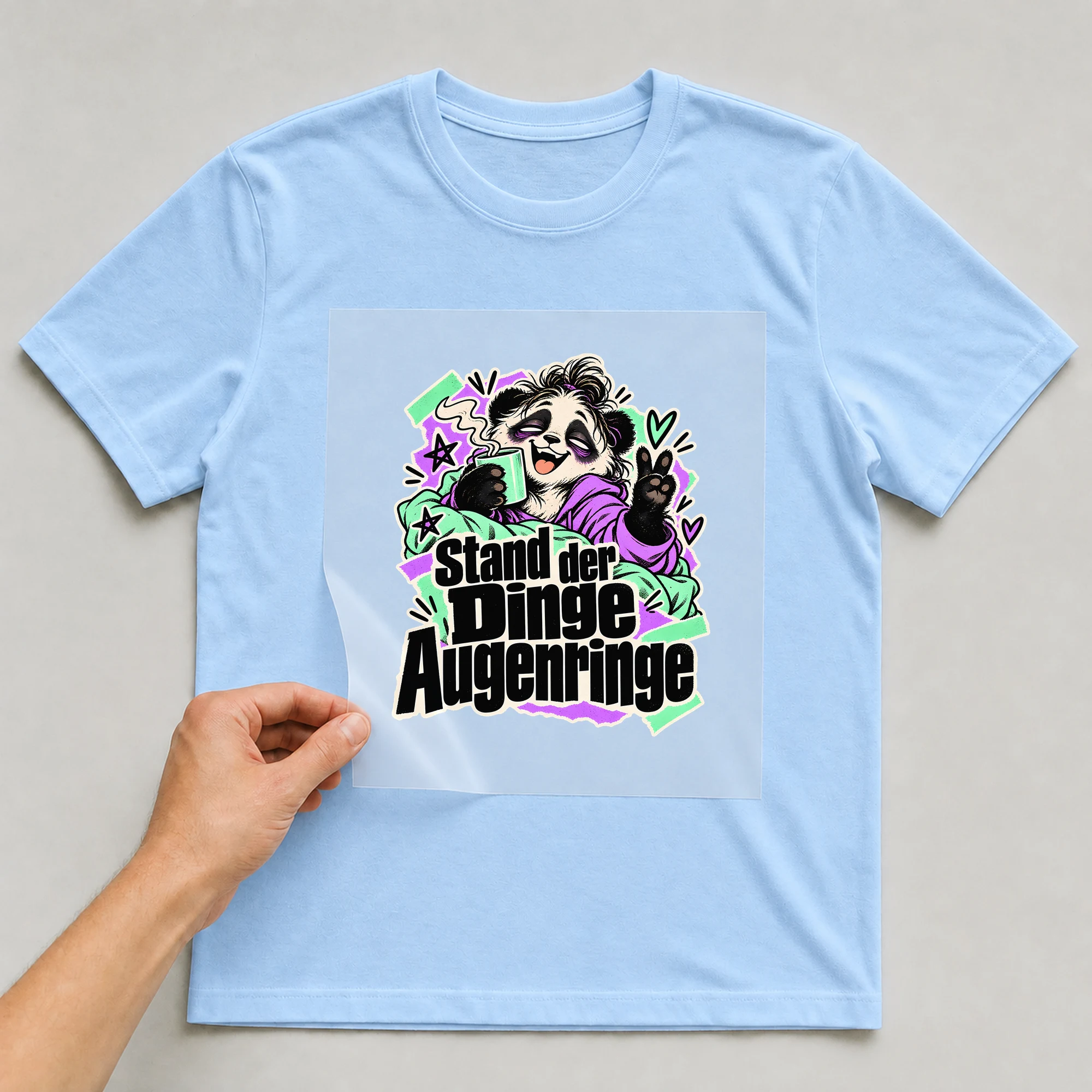 Bügelbild „Stand der Dinge Augenringe“ auf babyblauem T-Shirt, Folie wird aufgelegt