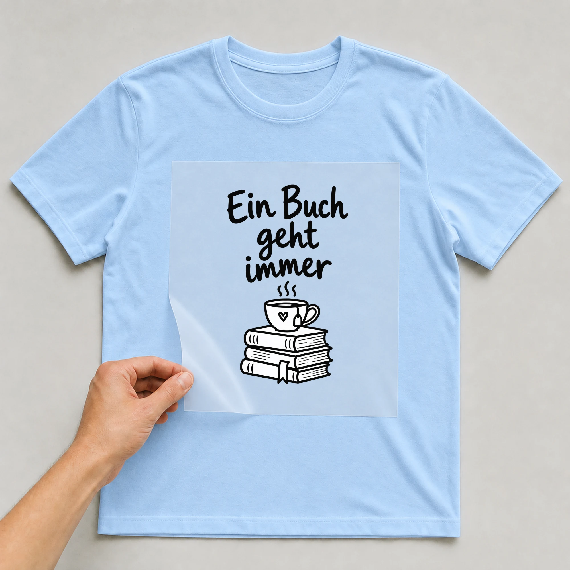 Bügelbild „Ein Buch geht immer“ auf babyblauem T-Shirt, Folie wird aufgelegt