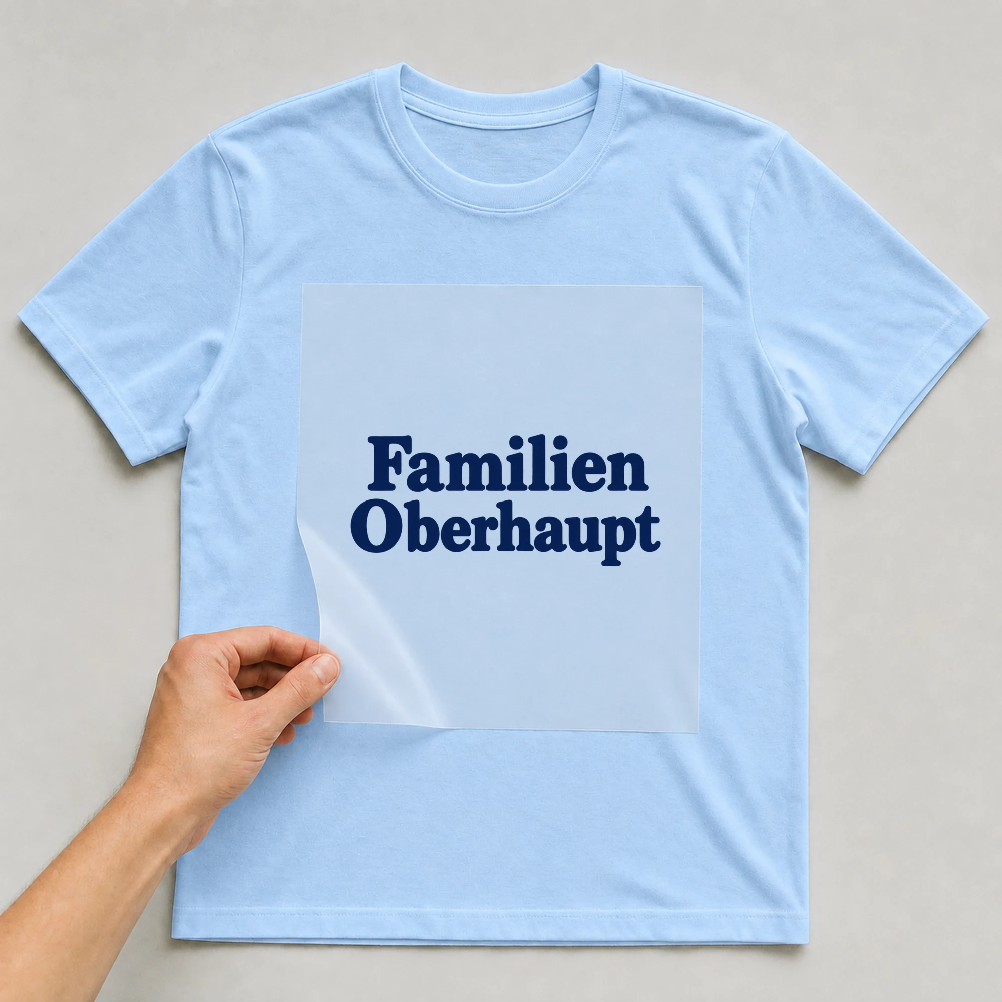 Bügelbild „Familien Oberhaupt“ auf babyblauem T-Shirt, Folie wird aufgelegt