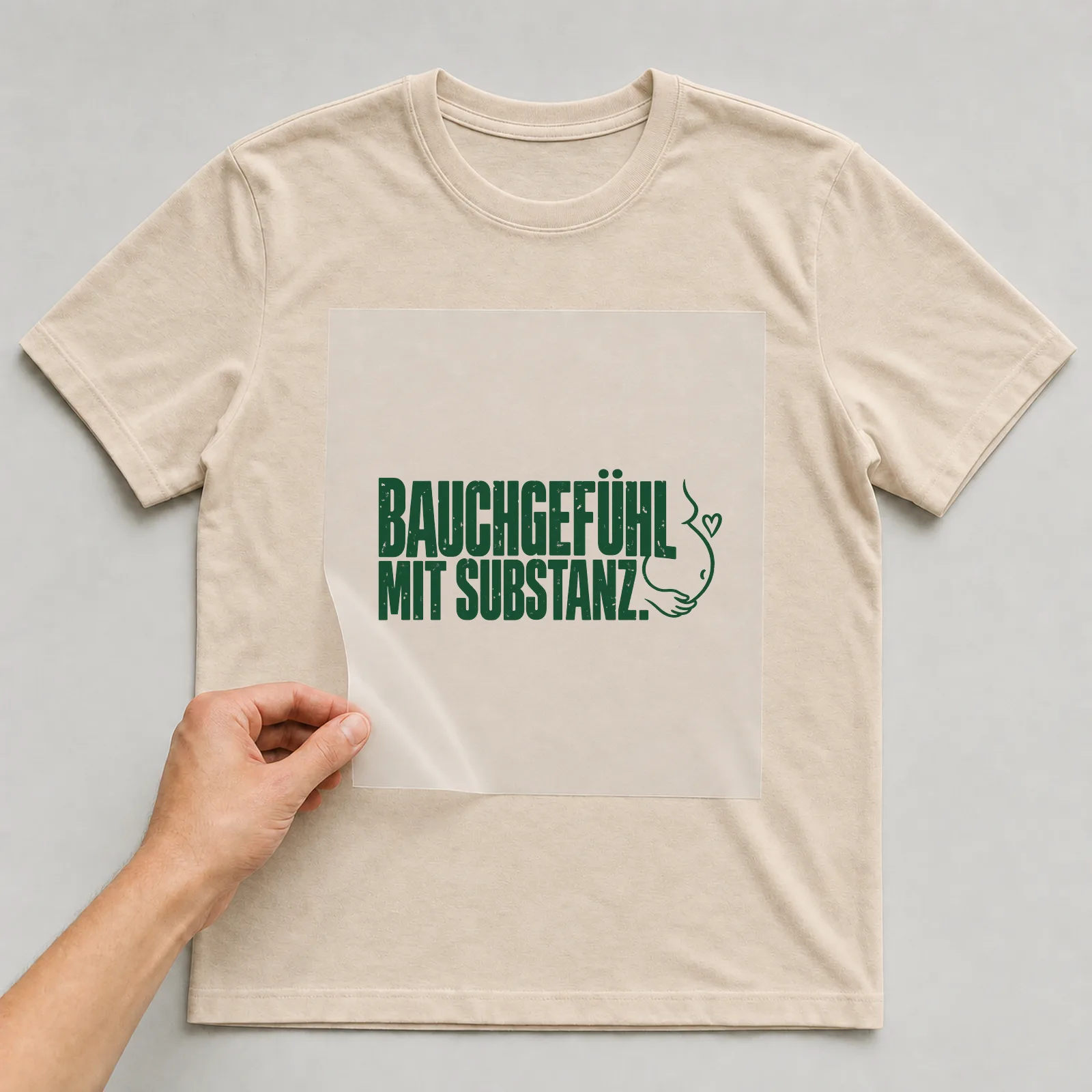 Bügelbild „Bauchgefühl mit Substanz“ auf beigem T-Shirt, Folie wird aufgelegt