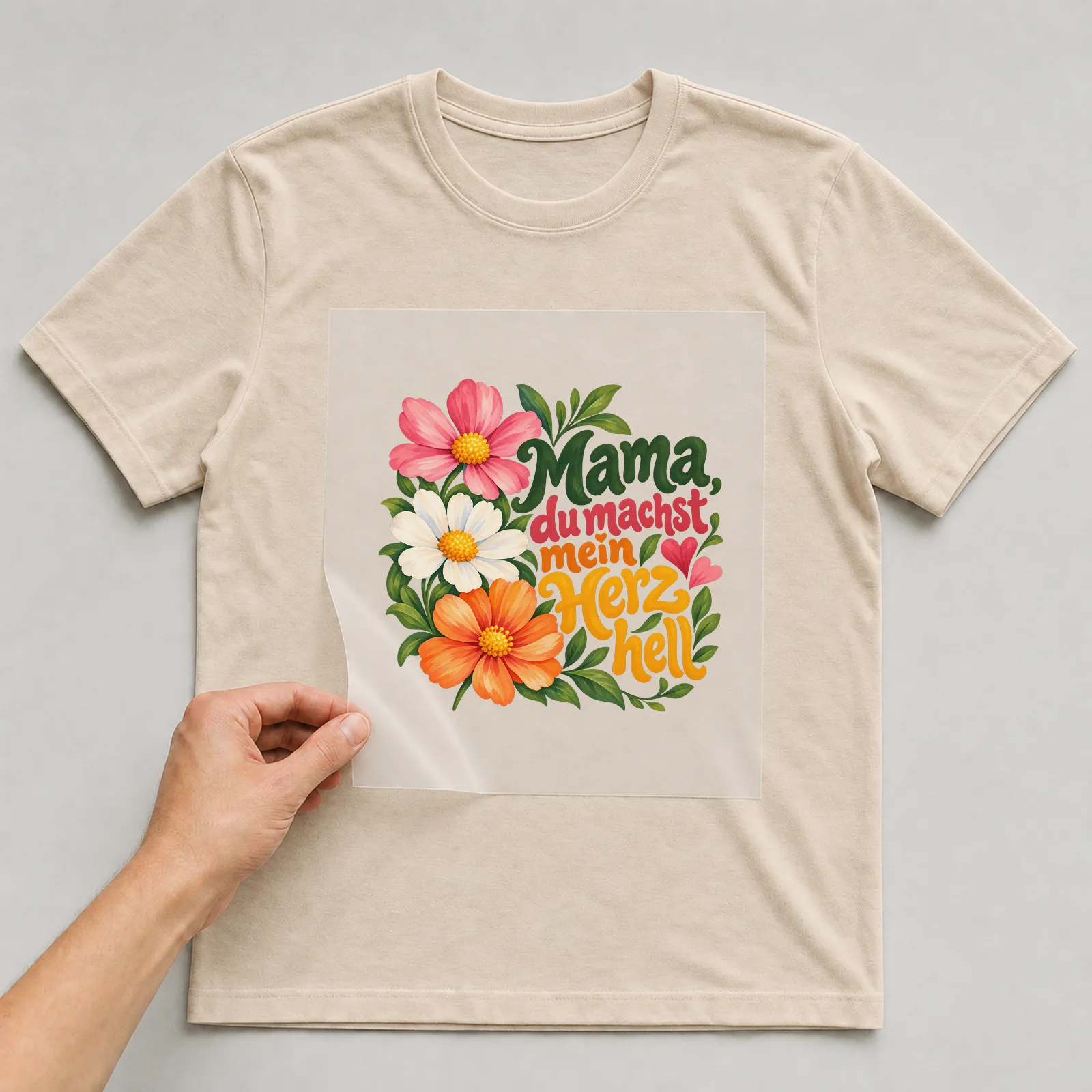 Bügelbild „Mama, du machst mein Herz hell“ auf beigem T-Shirt, Folie wird aufgelegt