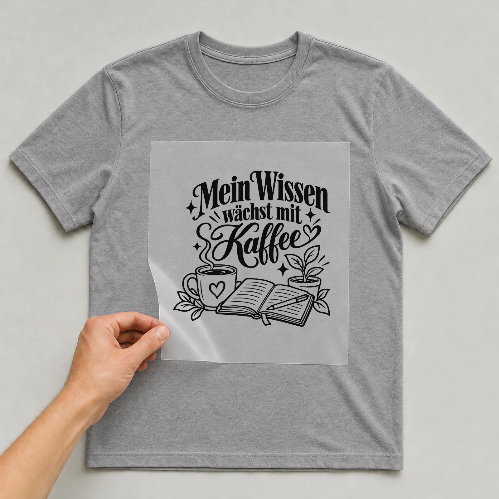 Bügelbild „Mein Wissen wächst mit Kaffee“ auf grauem T-Shirt, Folie wird aufgelegt