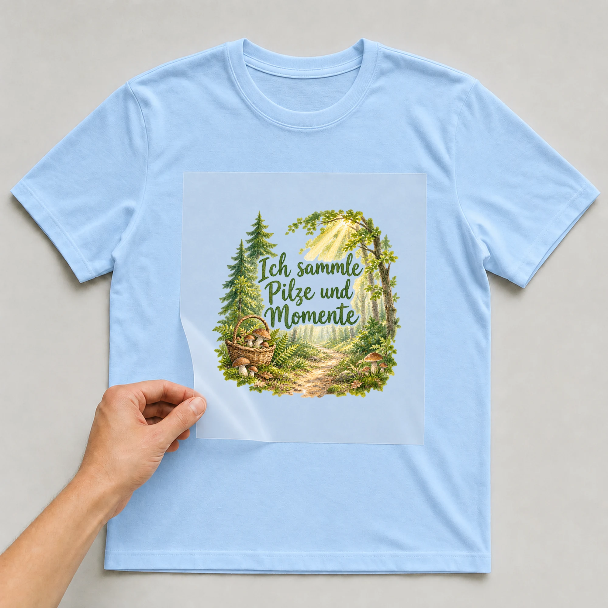 Bügelbild „Ich sammle Pilze und Momente“ auf babyblauem T-Shirt, Folie wird aufgelegt