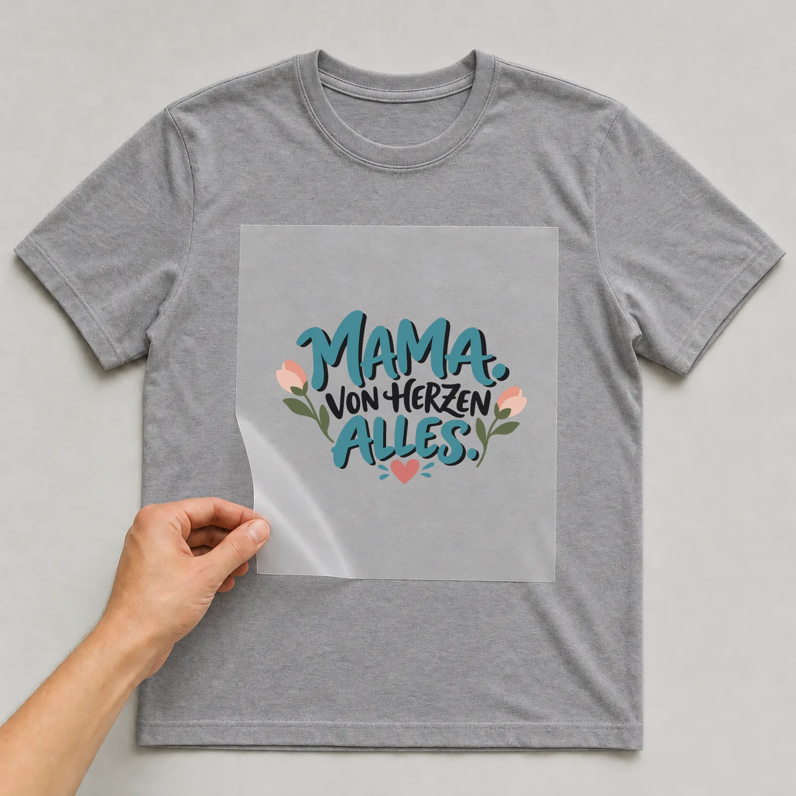 Bügelbild „Mama. Von Herzen alles.“ auf grauem T-Shirt, Folie wird aufgelegt