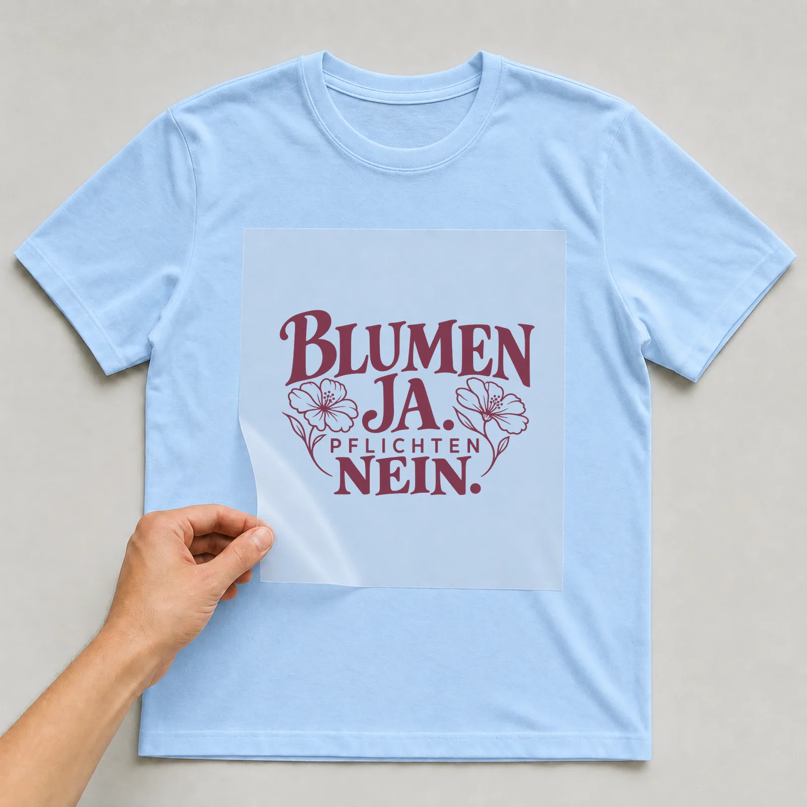 Bügelbild „Blumen ja. Pflichten nein.“ auf hellblauem T-Shirt, Folie wird aufgelegt