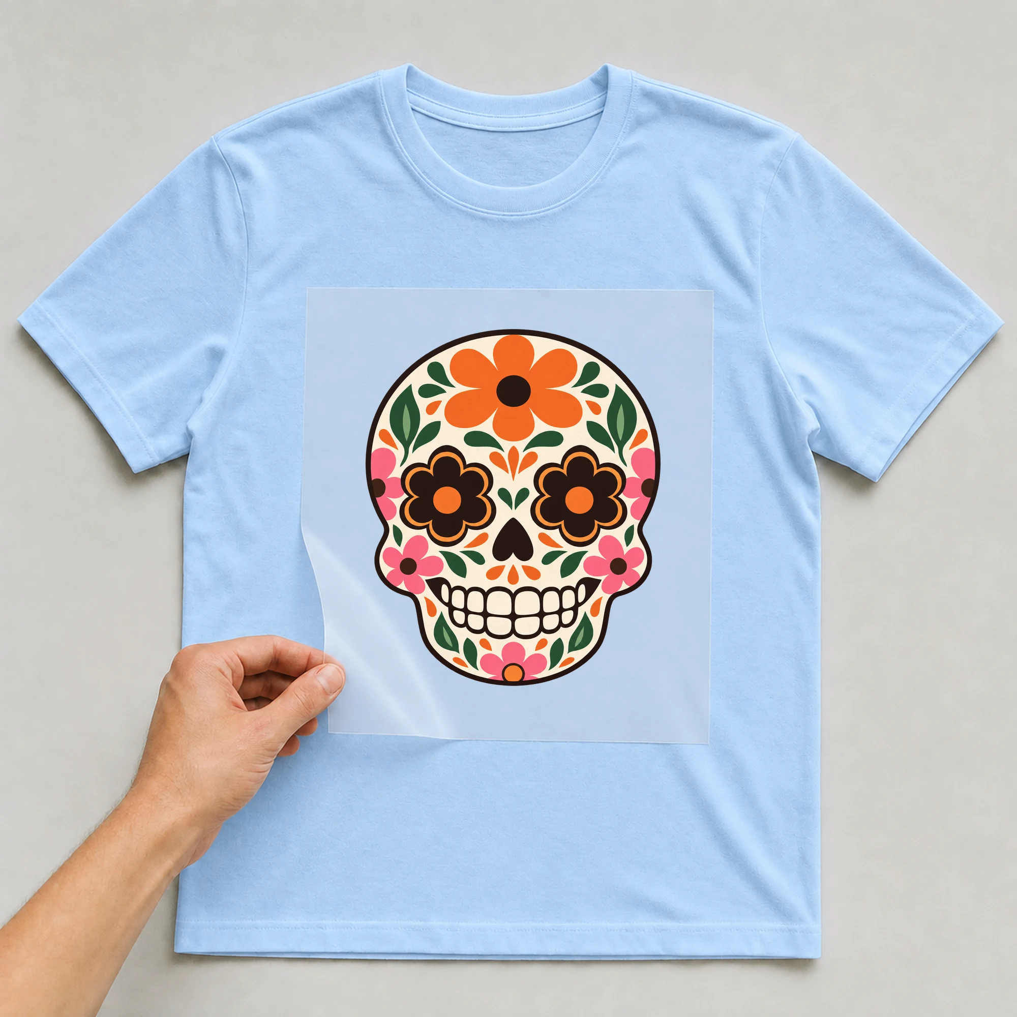 Bügelbild „Día de los Muertos Schädel“ auf babyblauem T-Shirt, Folie wird aufgelegt