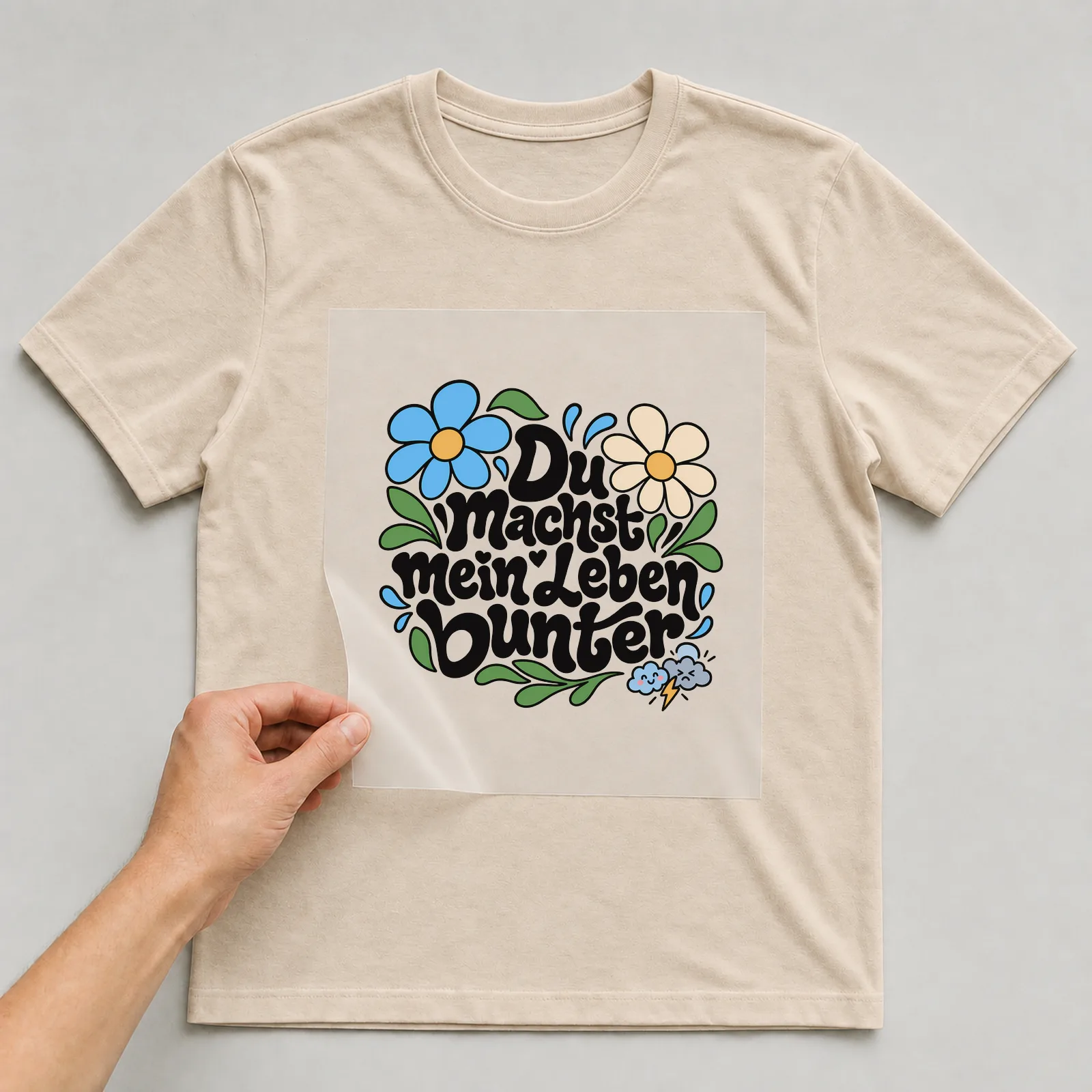 Bügelbild „Du machst mein Leben bunter“ (Blumenlettering) auf beigem T-Shirt, Folie wird aufgelegt