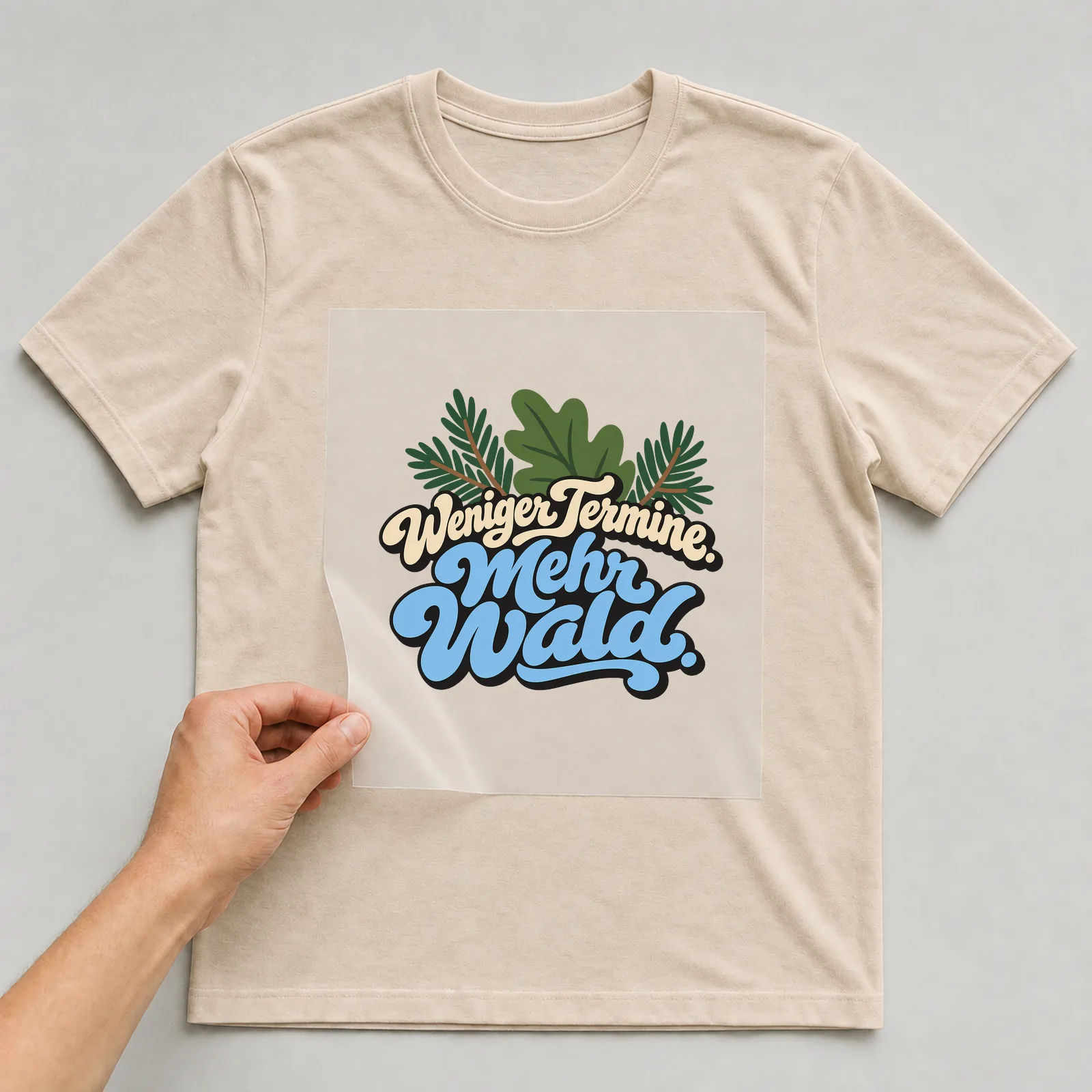 Bügelbild „Weniger Termine. Mehr Wald.“ auf beigem T-Shirt, Folie wird aufgelegt