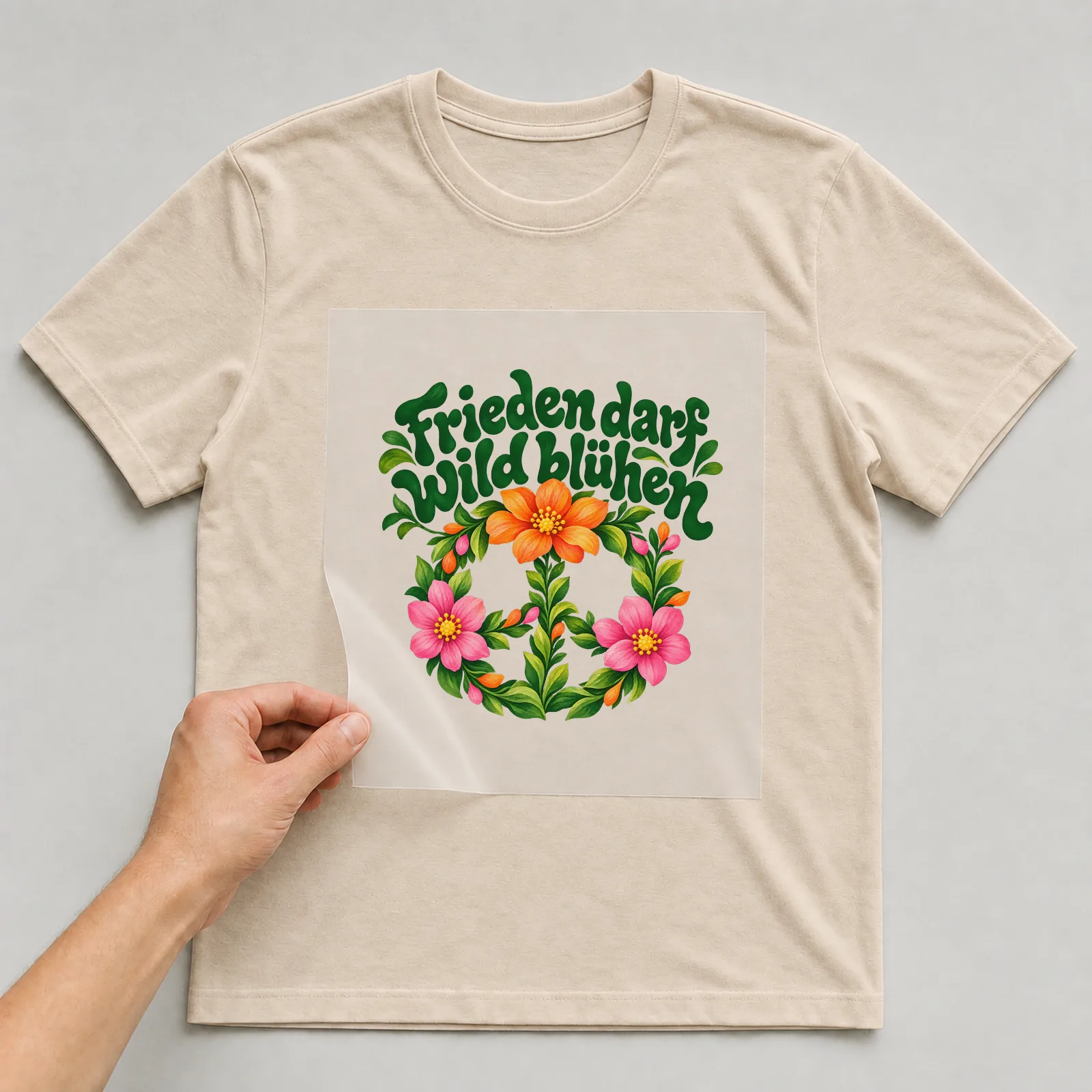 Bügelbild „Frieden darf wild blühen“ auf beigem T-Shirt, Folie wird aufgelegt