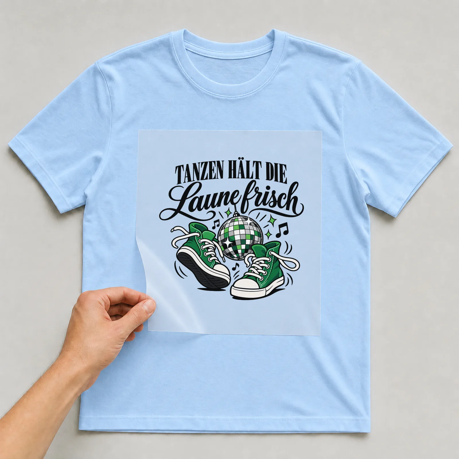 Bügelbild „Tanzen hält die Laune frisch“ auf hellblauem T-Shirt, Folie wird aufgelegt