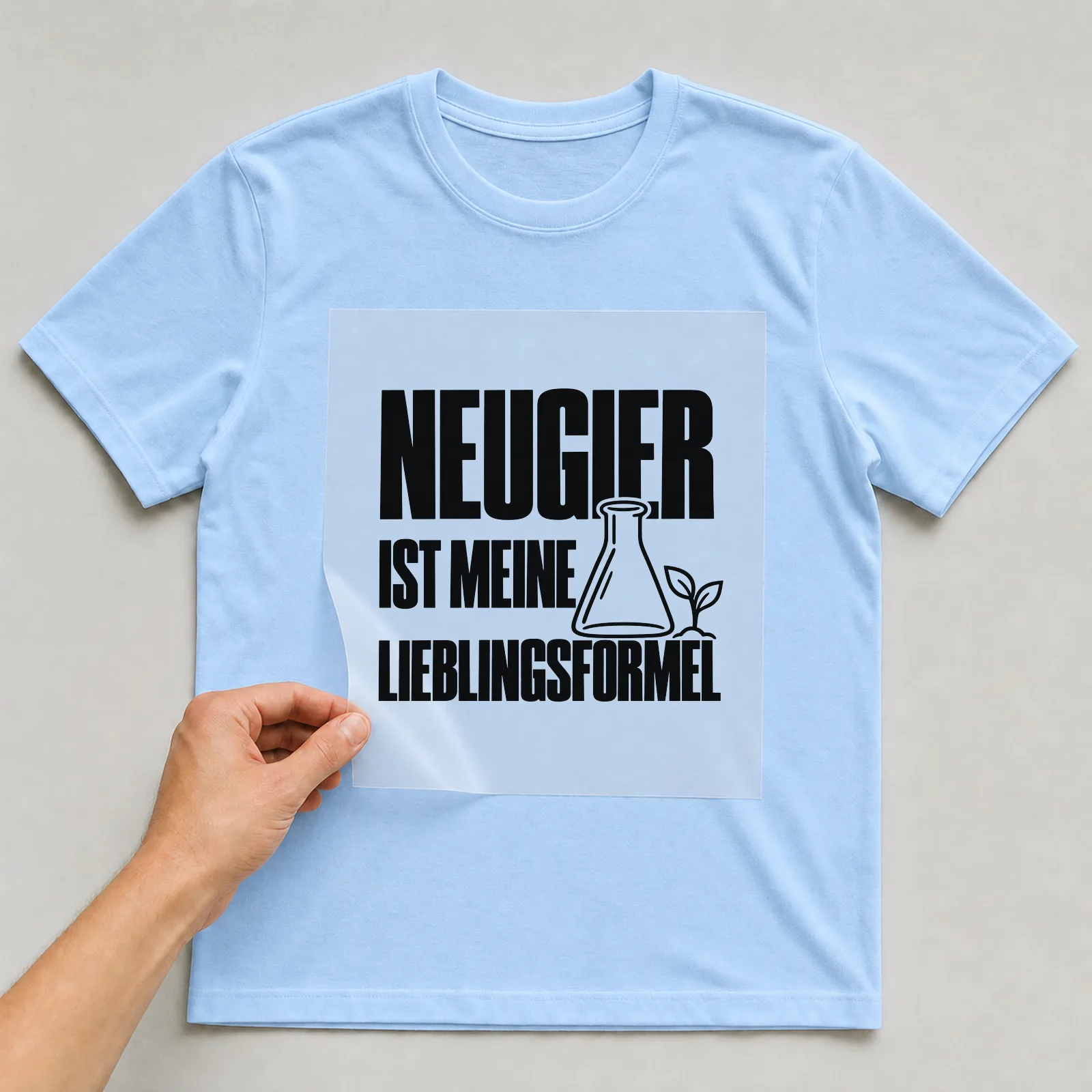 Bügelbild „Neugier ist meine Lieblingsformel“ auf hellblauem T-Shirt, Folie wird aufgelegt