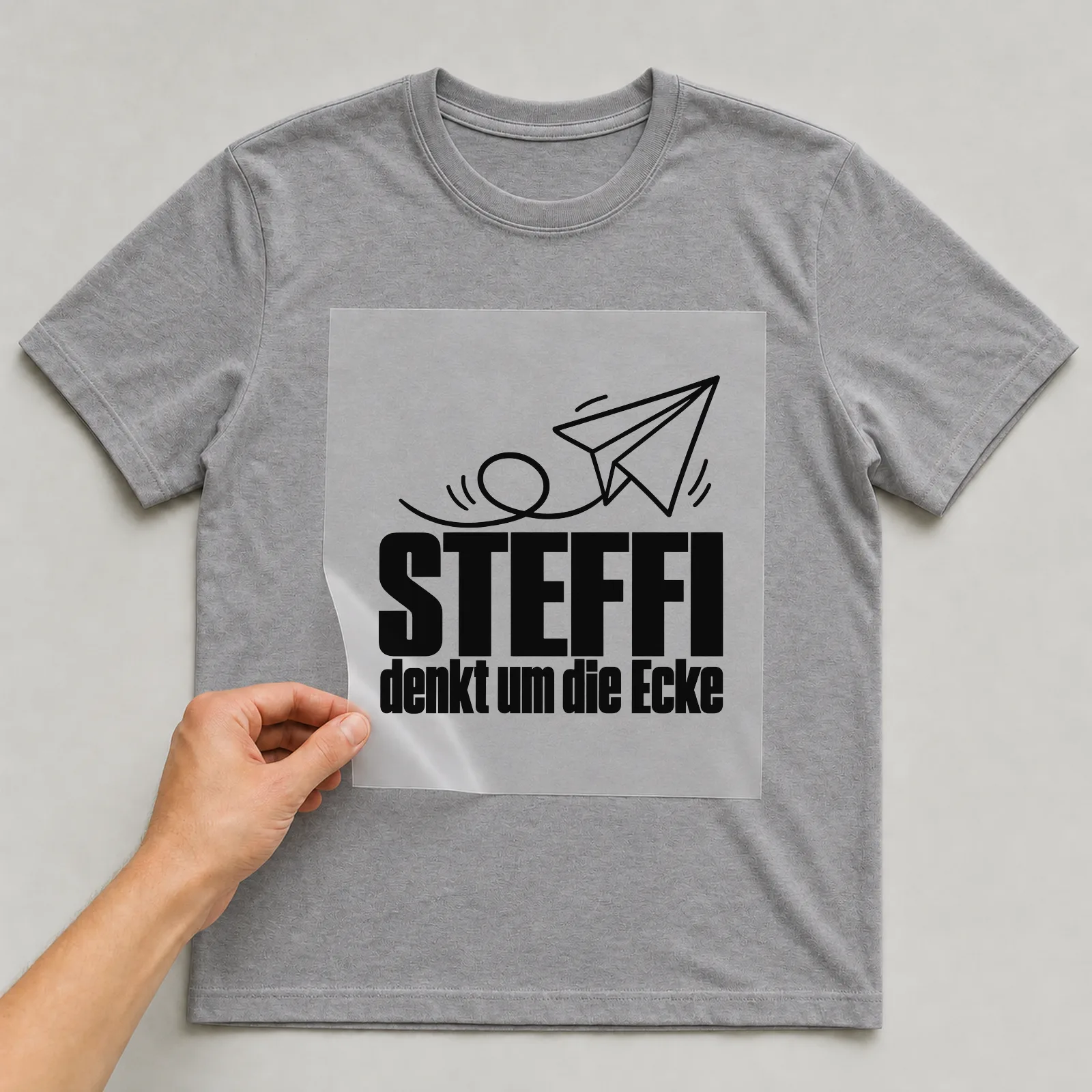 Bügelbild „Steffi denkt um die Ecke“ auf grauem T-Shirt, Folie wird aufgelegt
