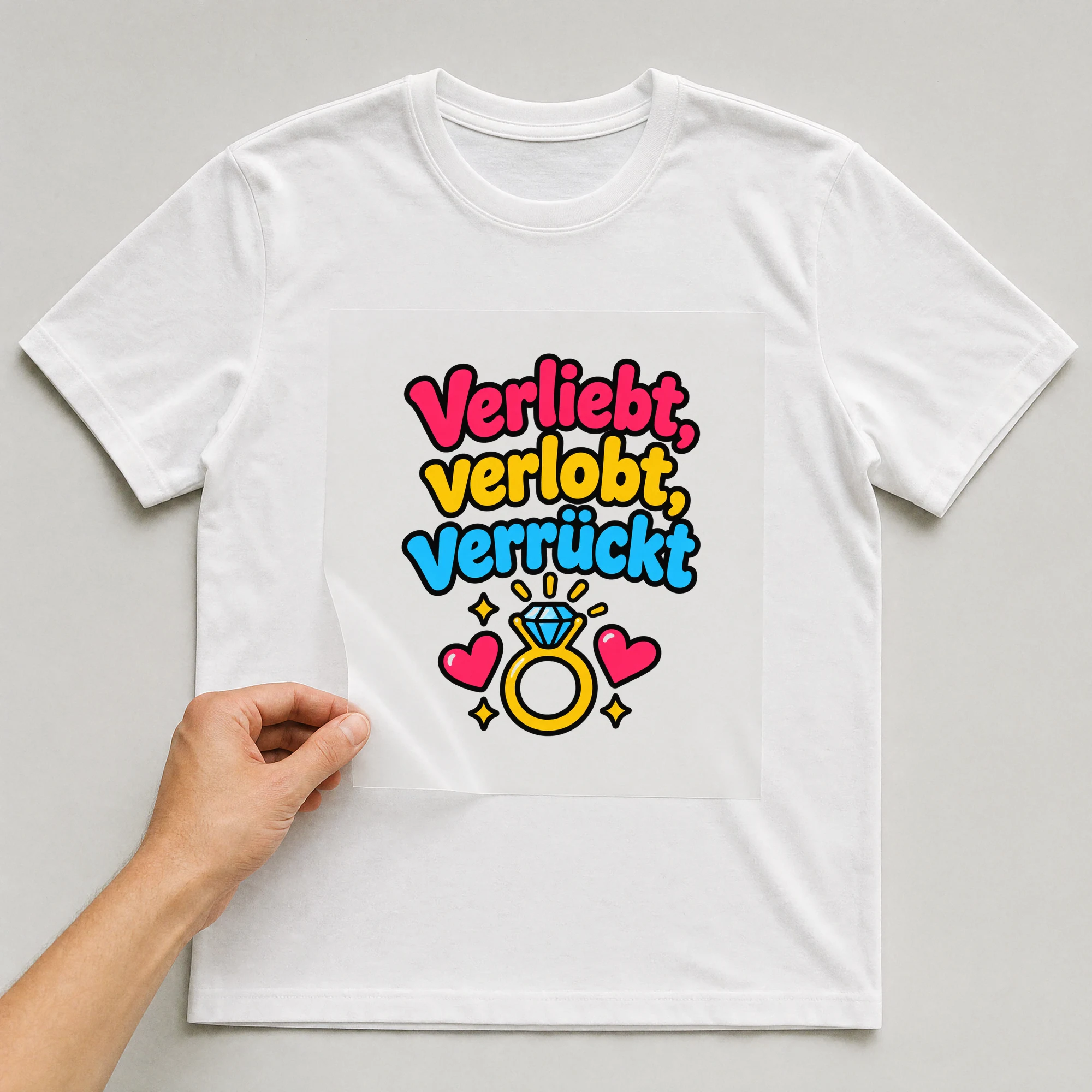 Bügelbild „Verliebt, verlobt, verrückt“ auf weißem T-Shirt, Folie wird aufgelegt