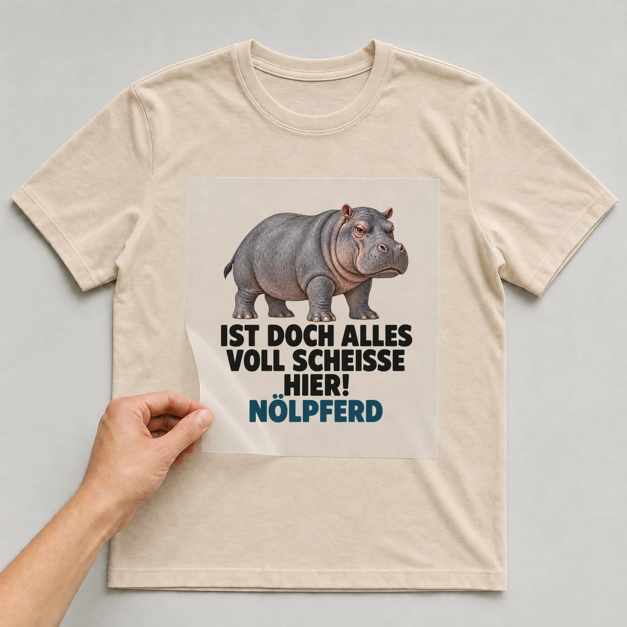 Bügelbild „Ist doch alles voll Sch*isse hier! Nölpferd“ auf beigem T-Shirt, Folie wird aufgelegt