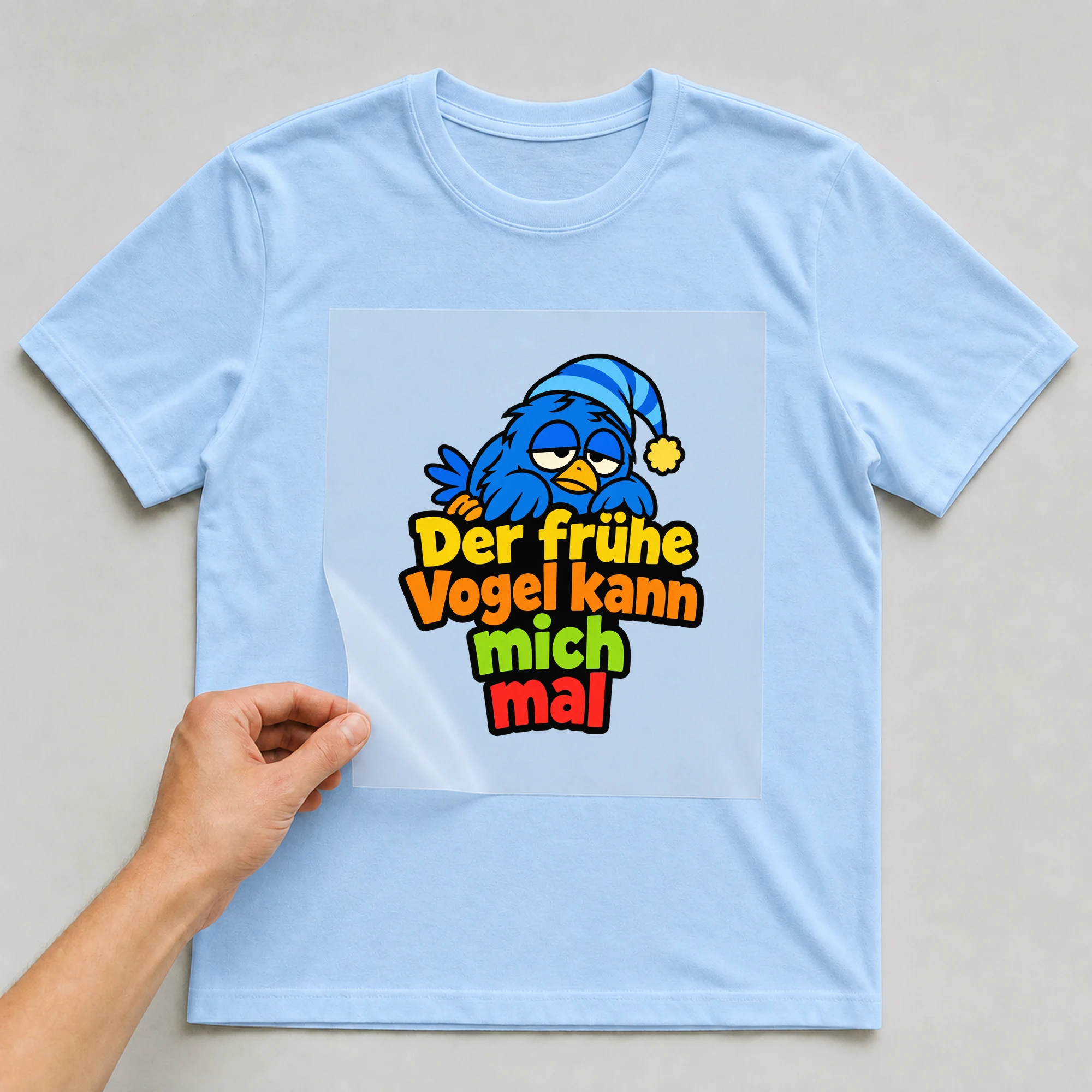 Bügelbild „Der frühe Vogel kann mich mal“ auf babyblauem T-Shirt, Folie wird aufgelegt