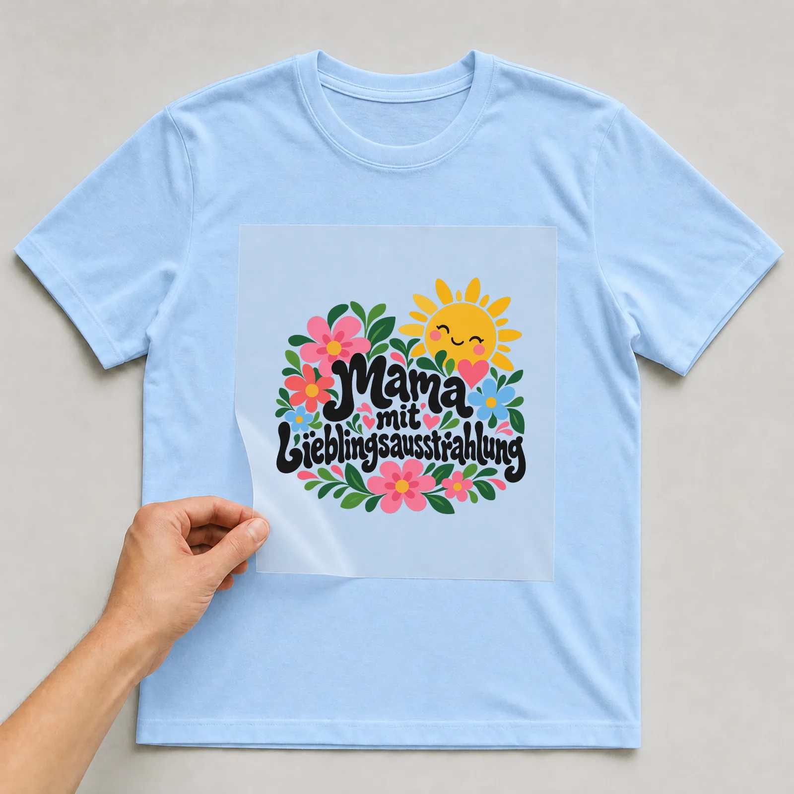 Bügelbild „Mama mit Lieblingsausstrahlung“ auf hellblauem T-Shirt, Folie wird aufgelegt
