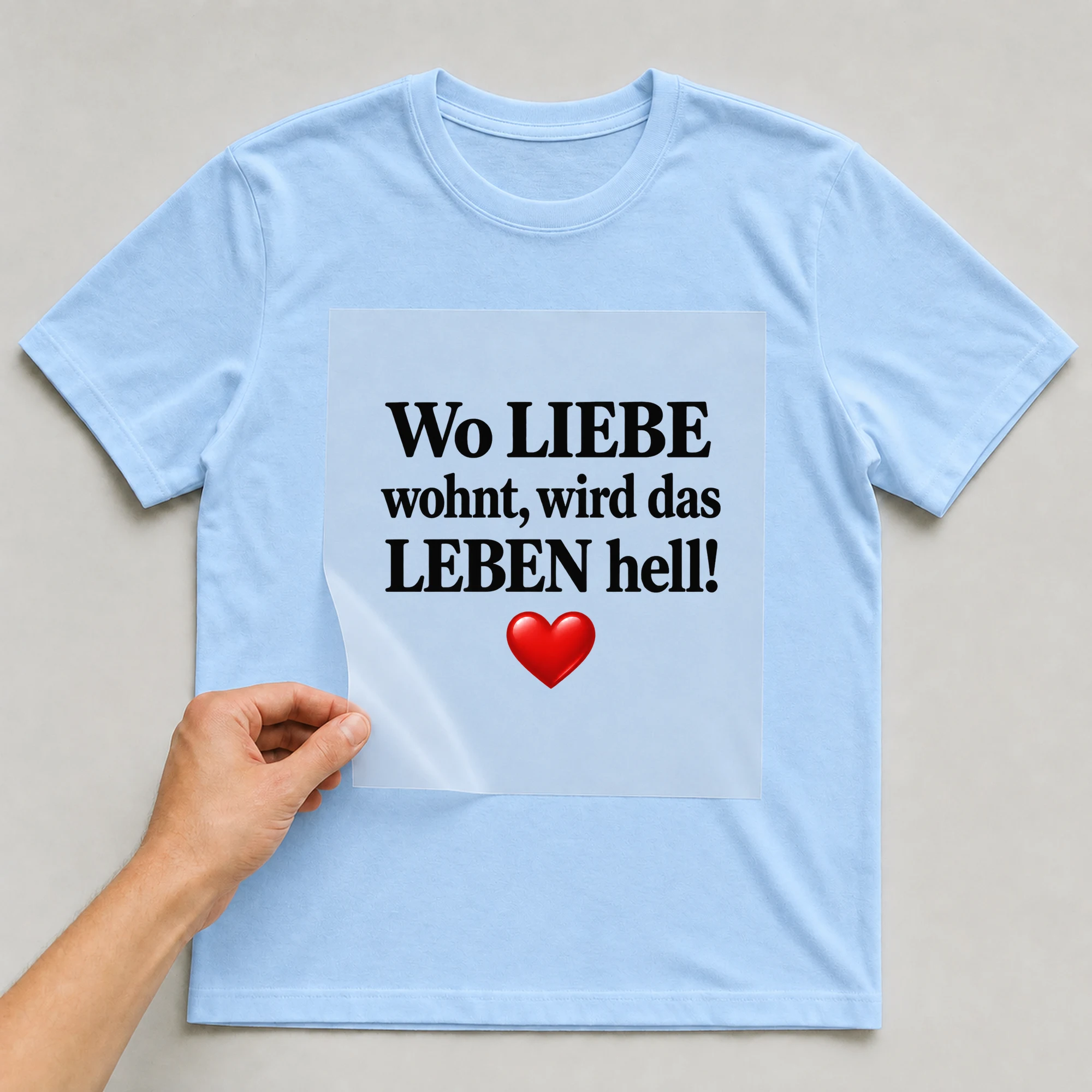 Bügelbild „Wo Liebe wohnt, wird das Leben hell!“ auf babyblauem T-Shirt, Folie wird aufgelegt
