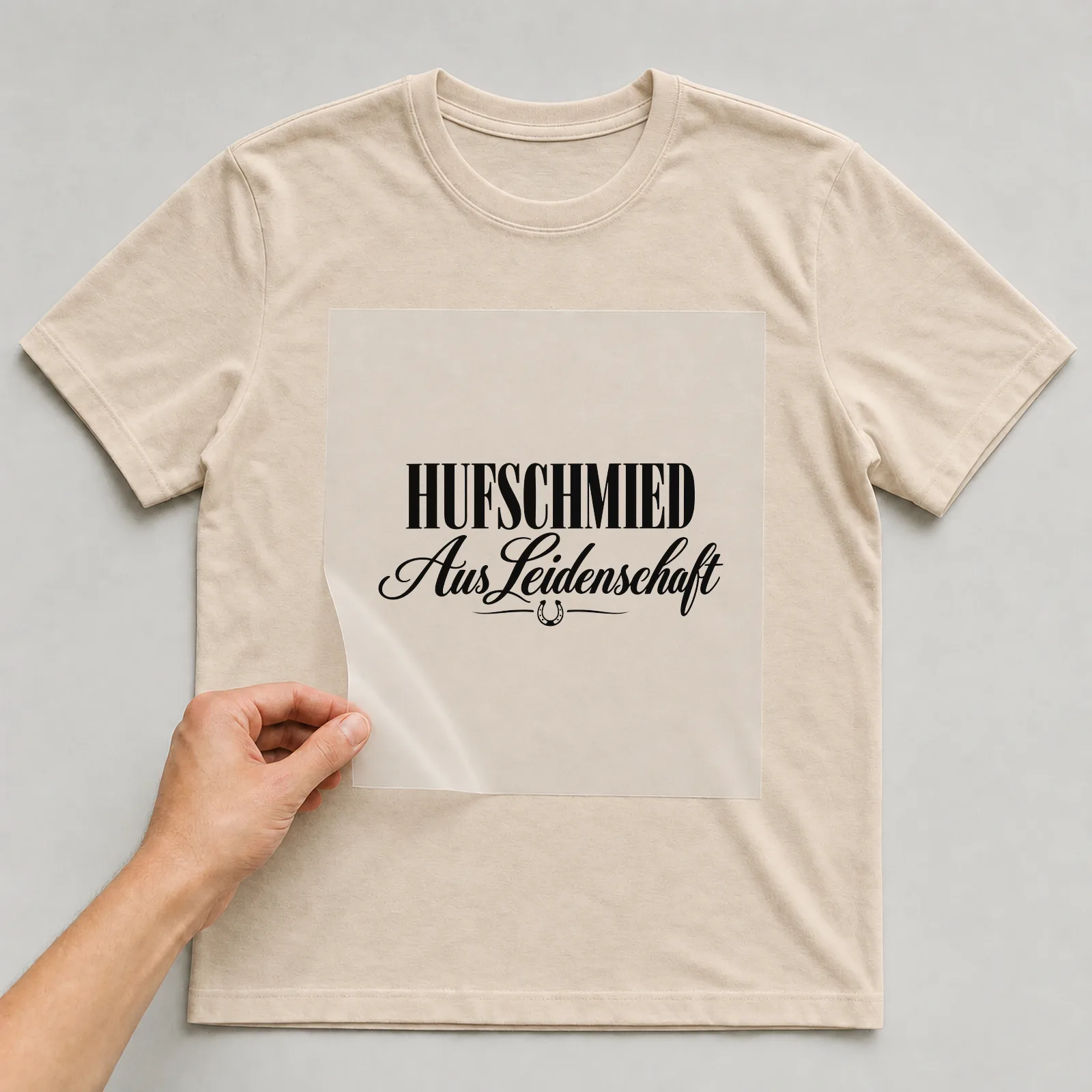 Bügelbild „Hufschmied aus Leidenschaft“ auf beigem T-Shirt, Folie wird aufgelegt