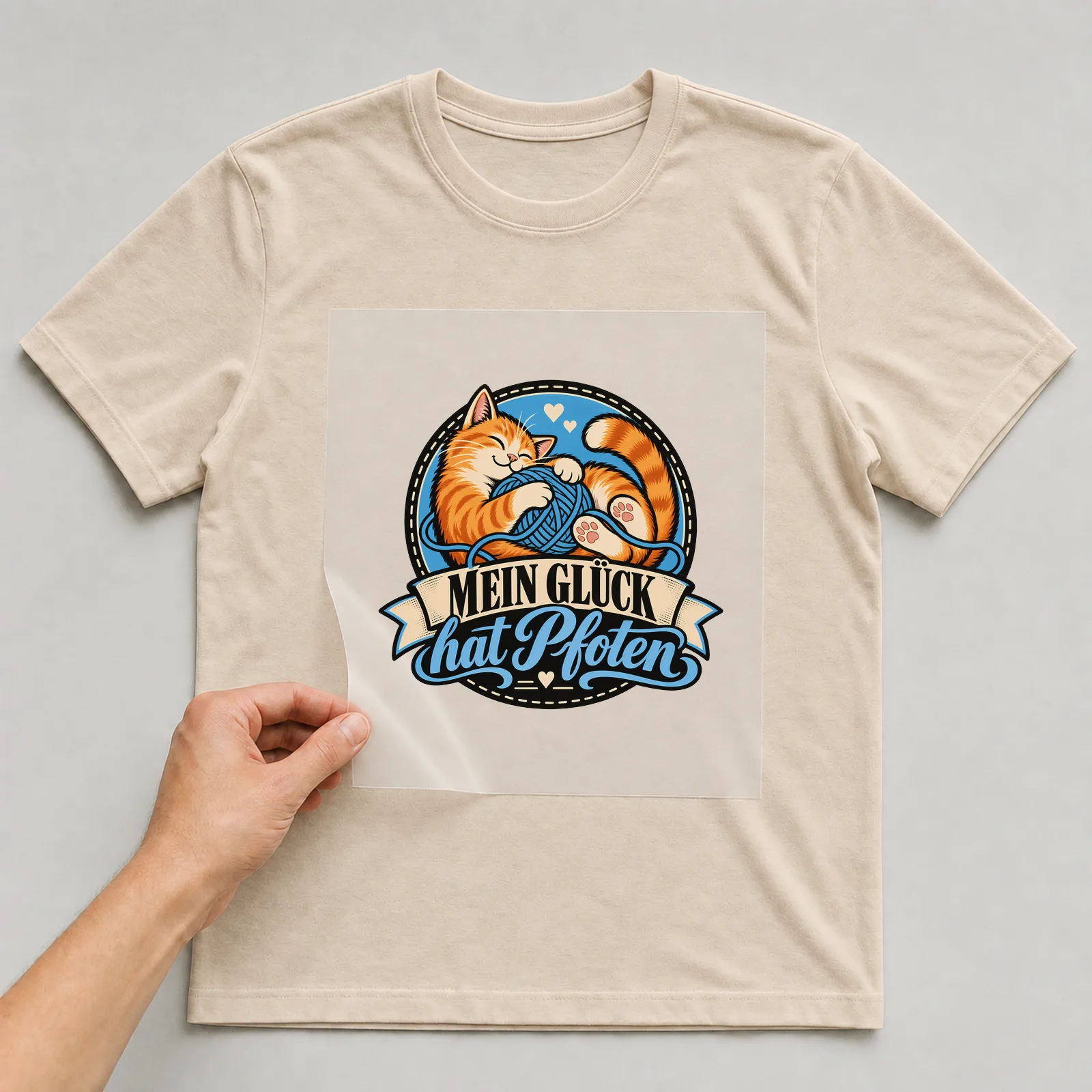 Bügelbild „Mein Glück hat Pfoten“ (Retro-Badge) auf beigem T-Shirt, Folie wird aufgelegt