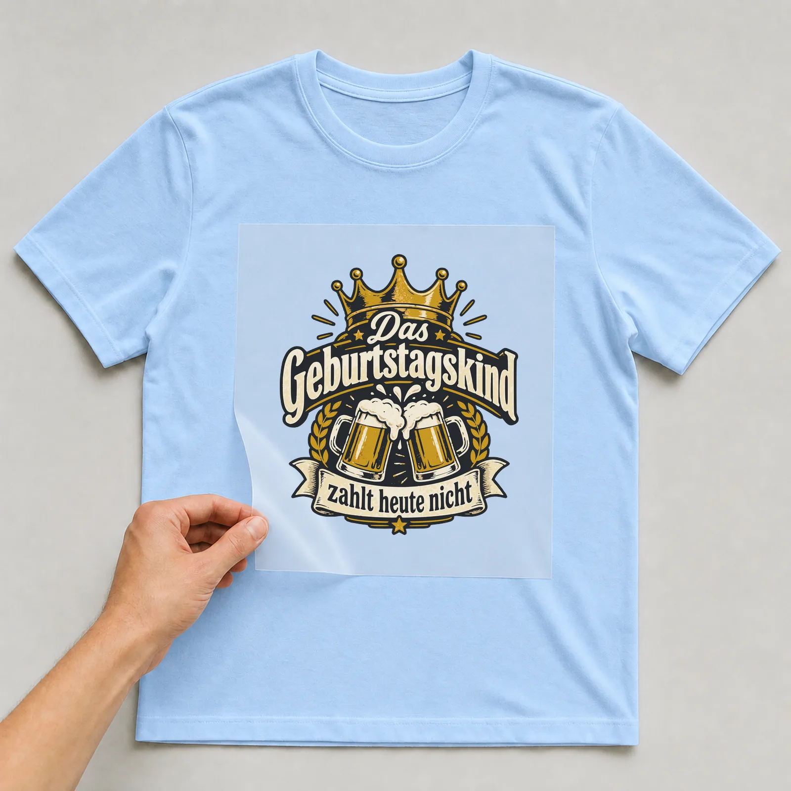 Bügelbild Das Geburtstagskind zahlt heute nicht auf hellblauem T-Shirt, Folie wird aufgelegt