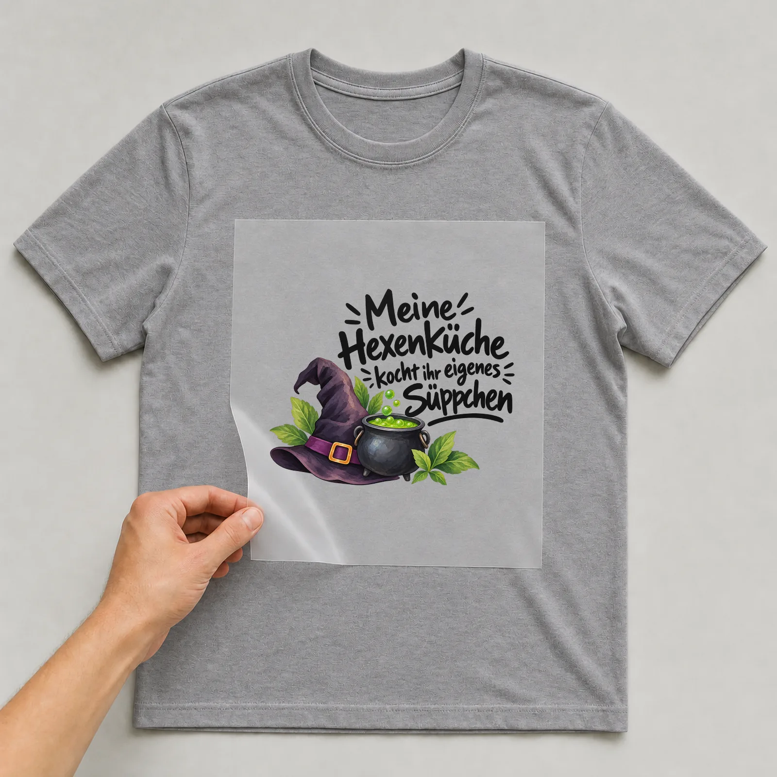 Bügelbild „Meine Hexenküche kocht ihr eigenes Süppchen“ auf grauem T-Shirt, Folie wird aufgelegt