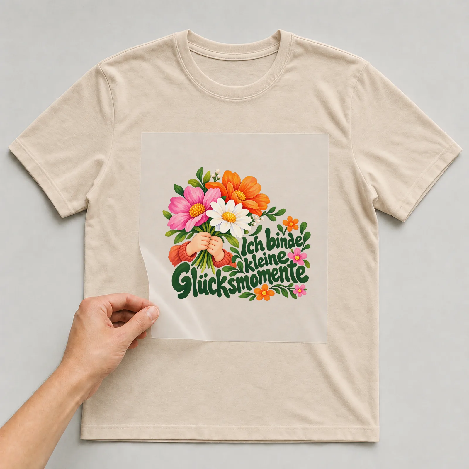 Bügelbild „Ich binde kleine Glücksmomente“ auf beigem T-Shirt, Folie wird aufgelegt
