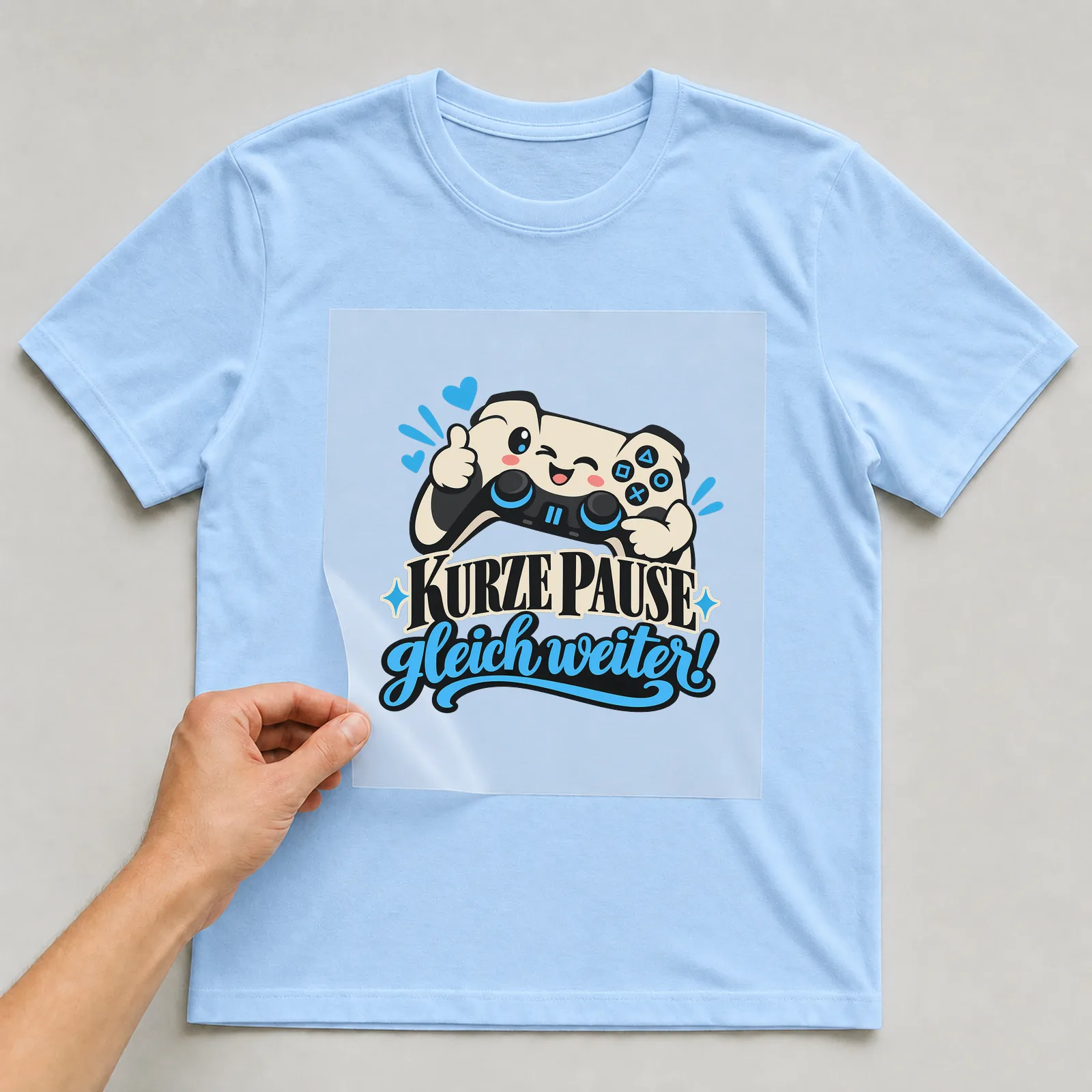 Bügelbild „Kurze Pause gleich weiter!“ auf hellblauem T-Shirt, Folie wird aufgelegt