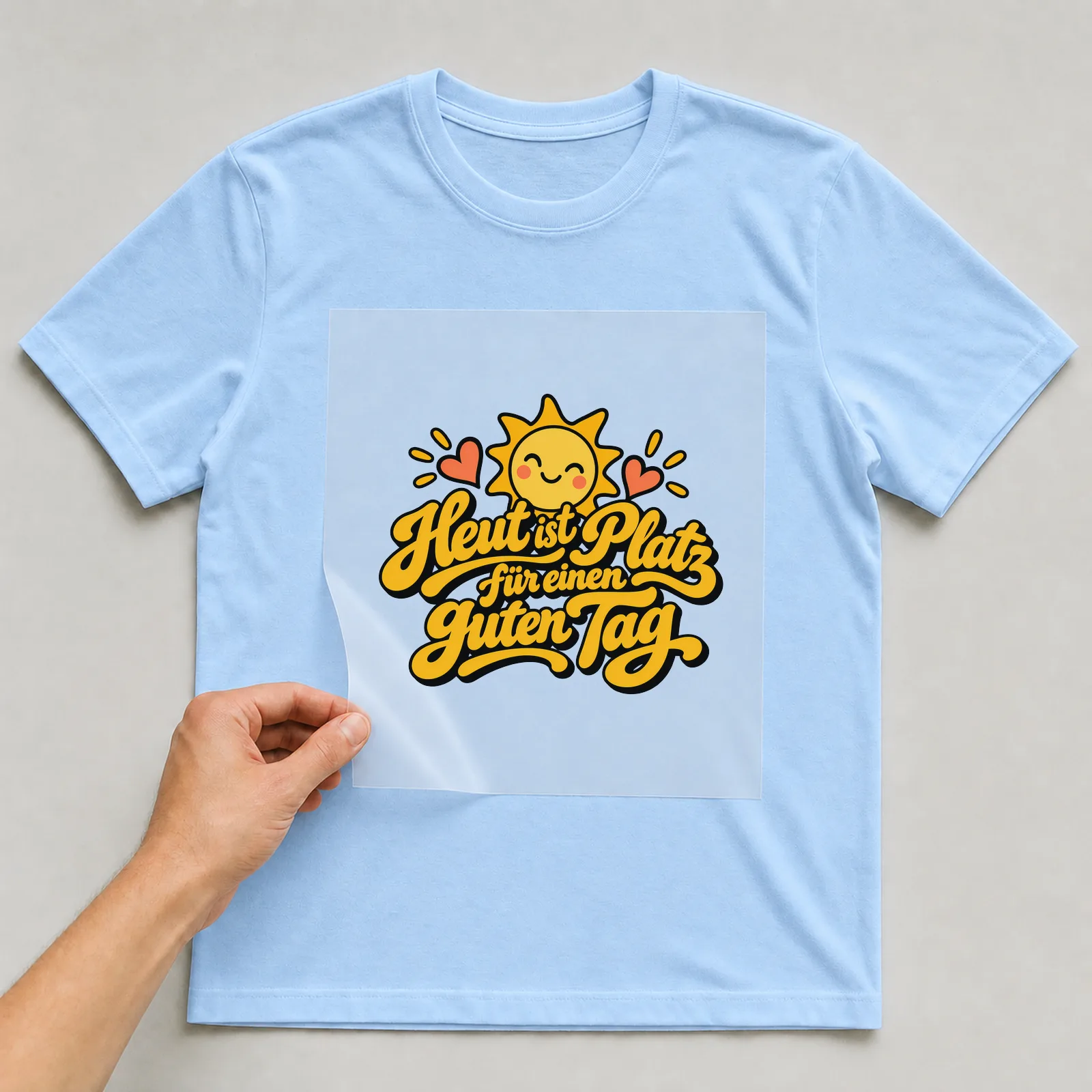 Bügelbild „Heut ist Platz für einen guten Tag“ auf hellblauem T-Shirt, Folie wird aufgelegt