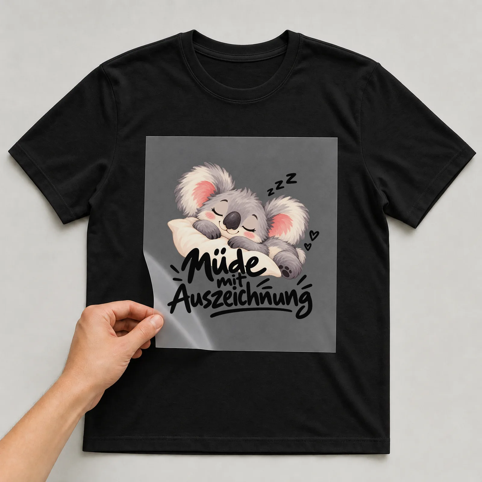Bügelbild „Müde mit Auszeichnung“ auf schwarzem T-Shirt, Folie wird aufgelegt