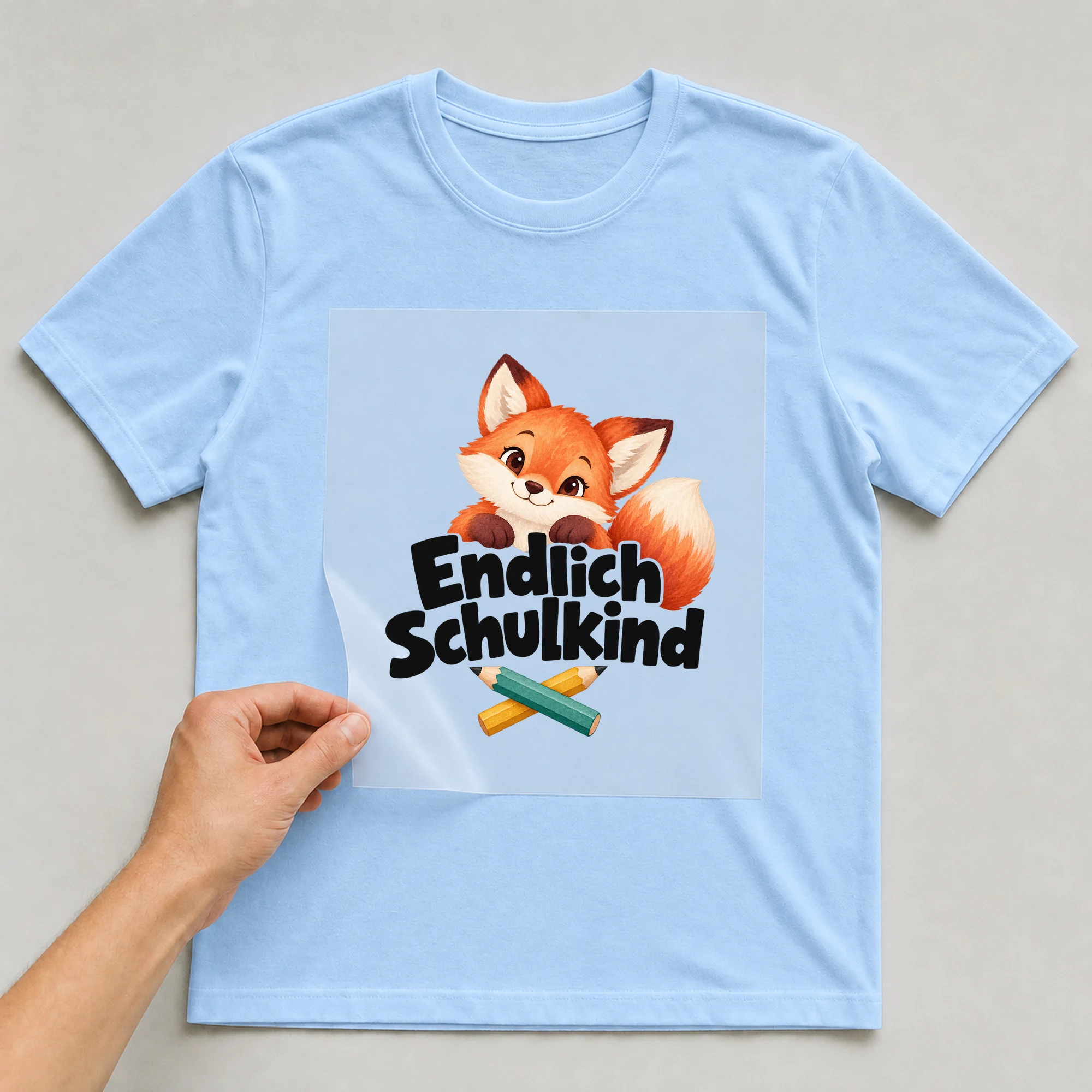 Bügelbild „Endlich Schulkind“ auf babyblauem T-Shirt, Folie wird aufgelegt