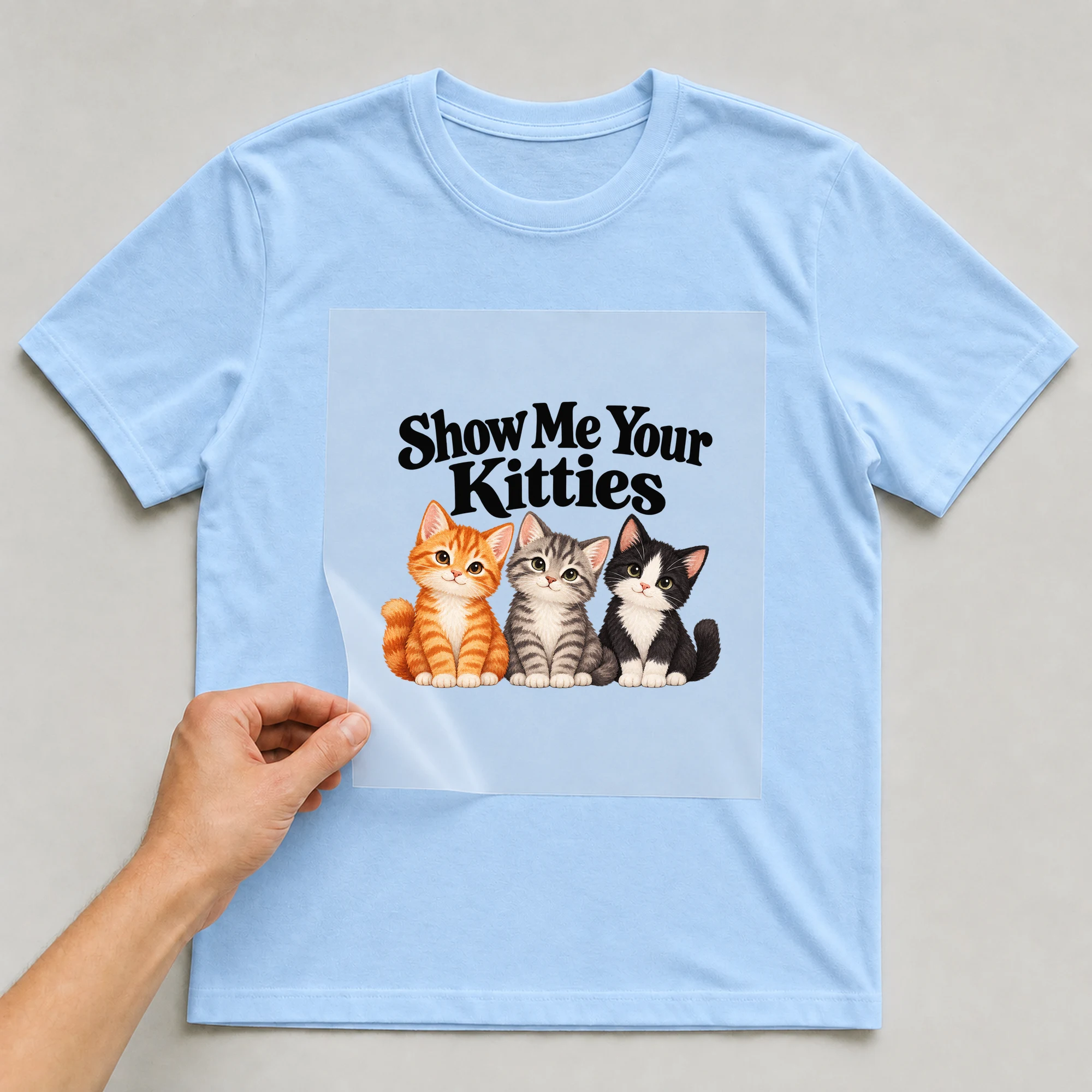 Bügelbild „Show Me Your Kitties“ auf babyblauem T-Shirt, Folie wird aufgelegt