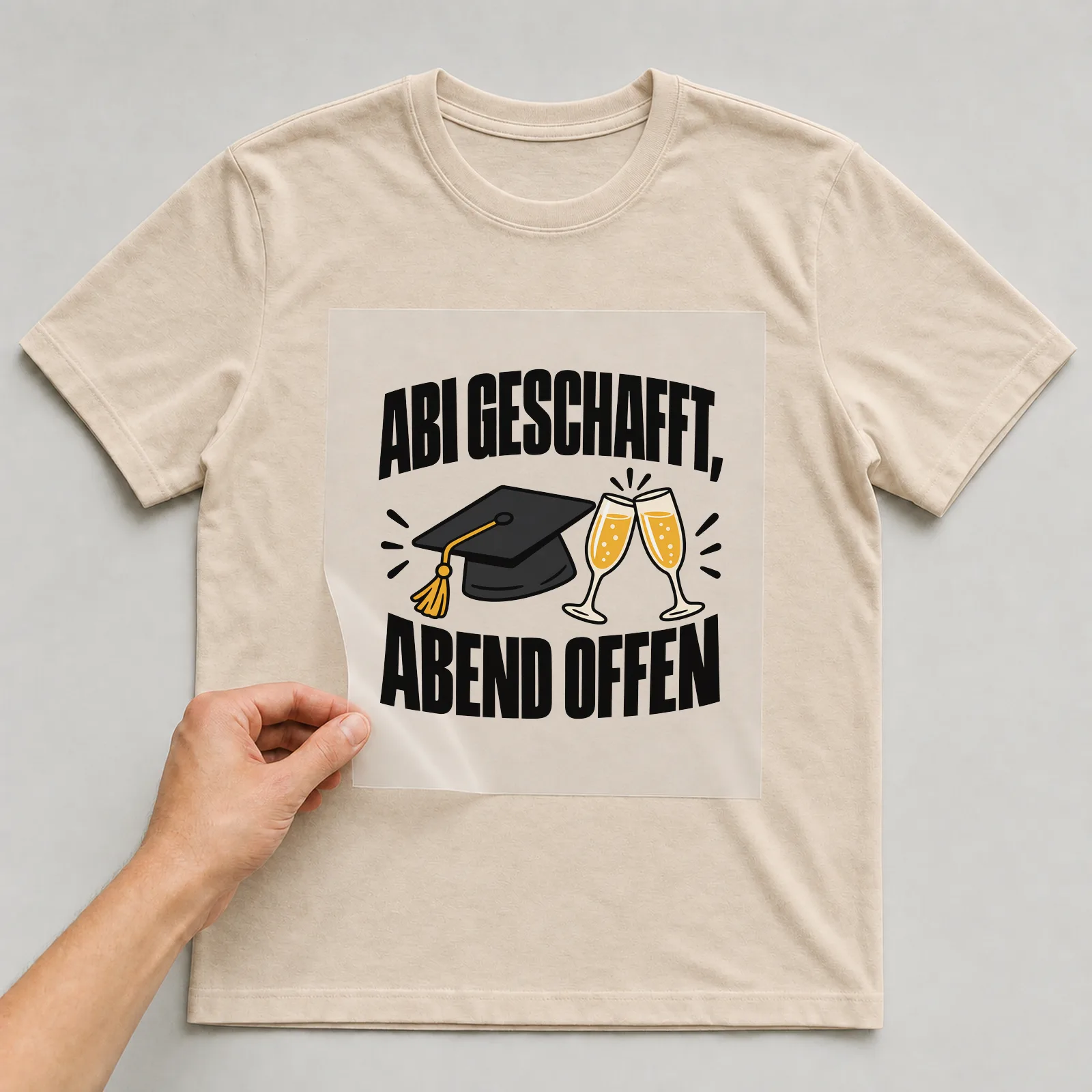 Bügelbild „Abi geschafft, Abend offen“ auf beigem T-Shirt, Folie wird aufgelegt