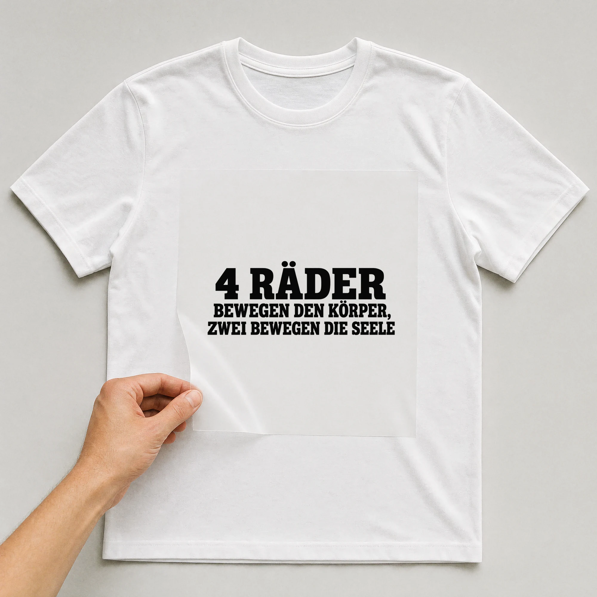 Bügelbild „4 Räder Bewegen Den Körper, Zwei Bewegen Die Seele“ auf weißem T-Shirt, Folie wird aufgelegt