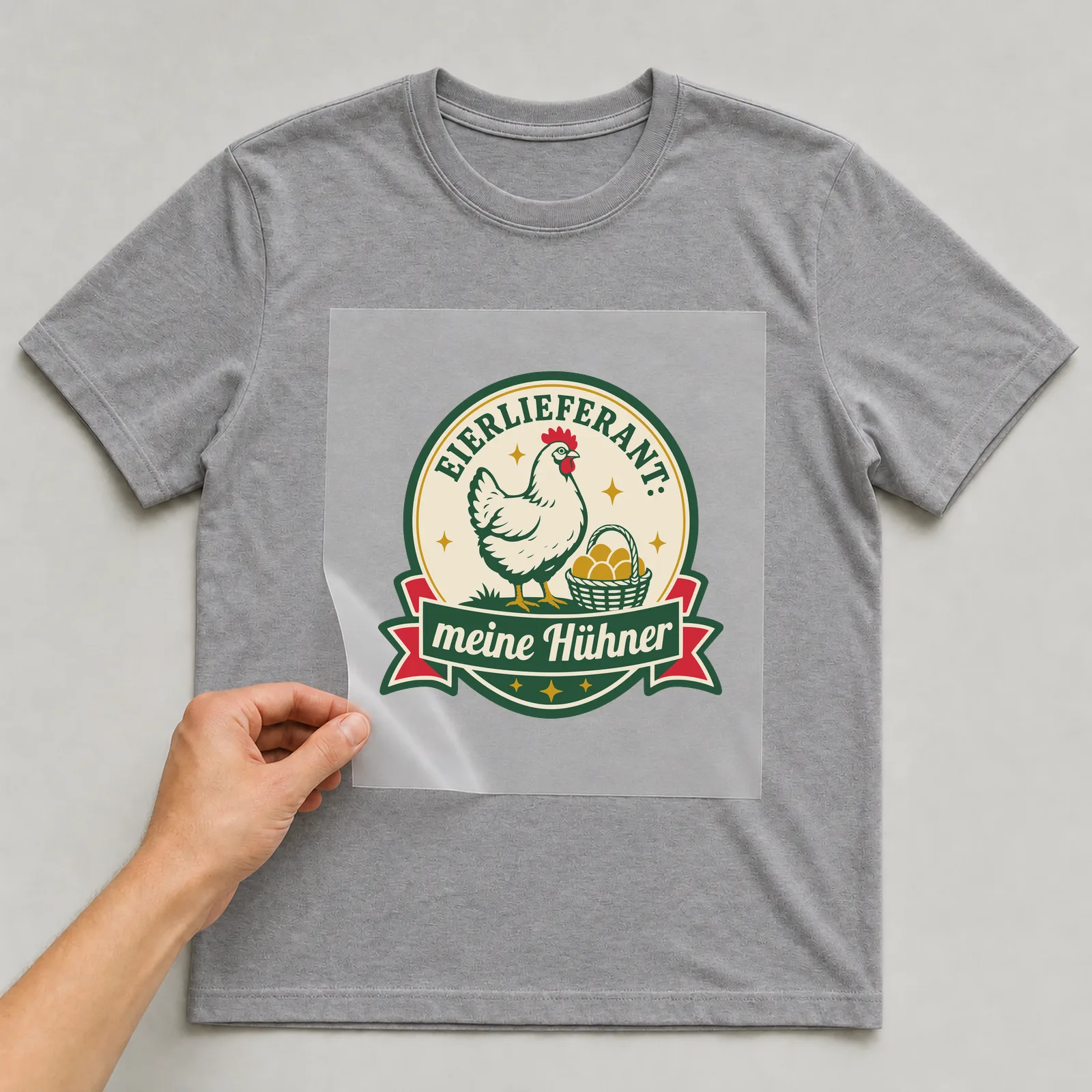 Bügelbild Eierlieferant: meine Hühner auf grauem T-Shirt, Folie wird aufgelegt