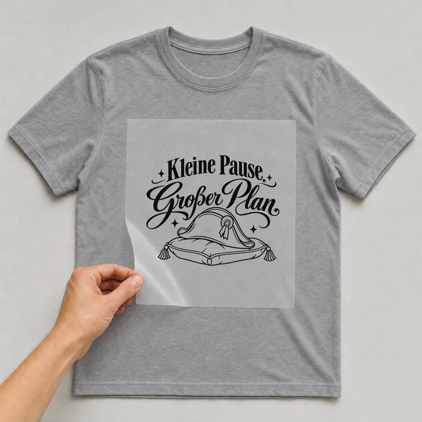 Bügelbild „Kleine Pause. Großer Plan.“ auf grauem T-Shirt, Folie wird aufgelegt