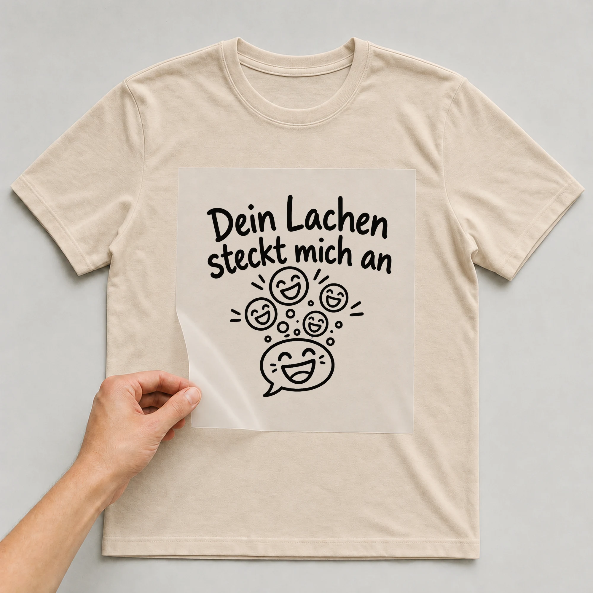 Bügelbild „Dein Lachen steckt mich an“ auf beigem T-Shirt, Folie wird aufgelegt