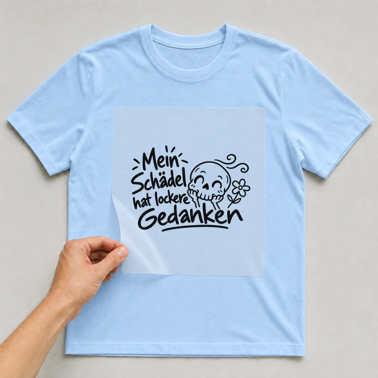 Bügelbild „Mein Schädel hat lockere Gedanken“ auf hellblauem T-Shirt, Folie wird aufgelegt