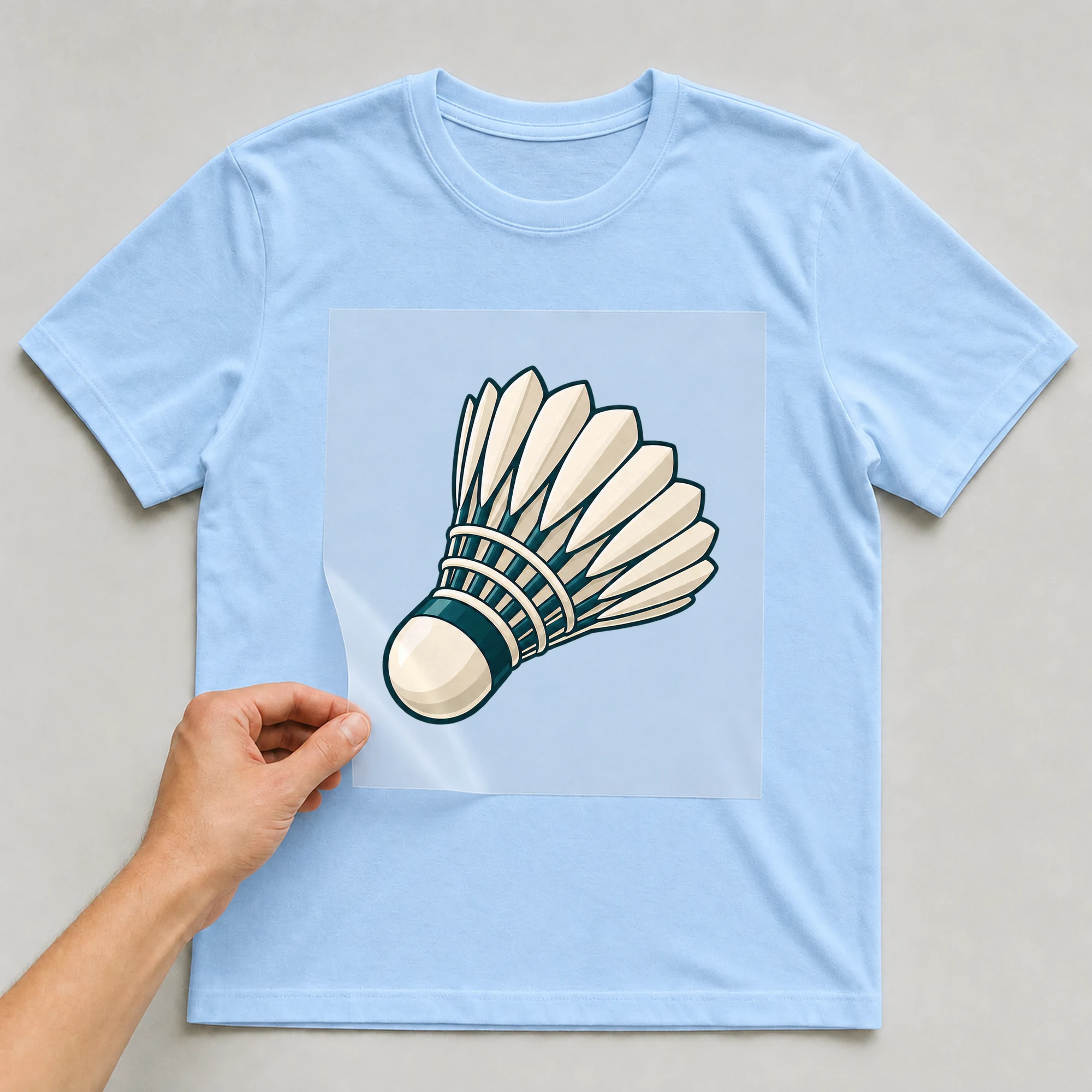 Bügelbild „Federball“ auf babyblauem T-Shirt, Folie wird aufgelegt