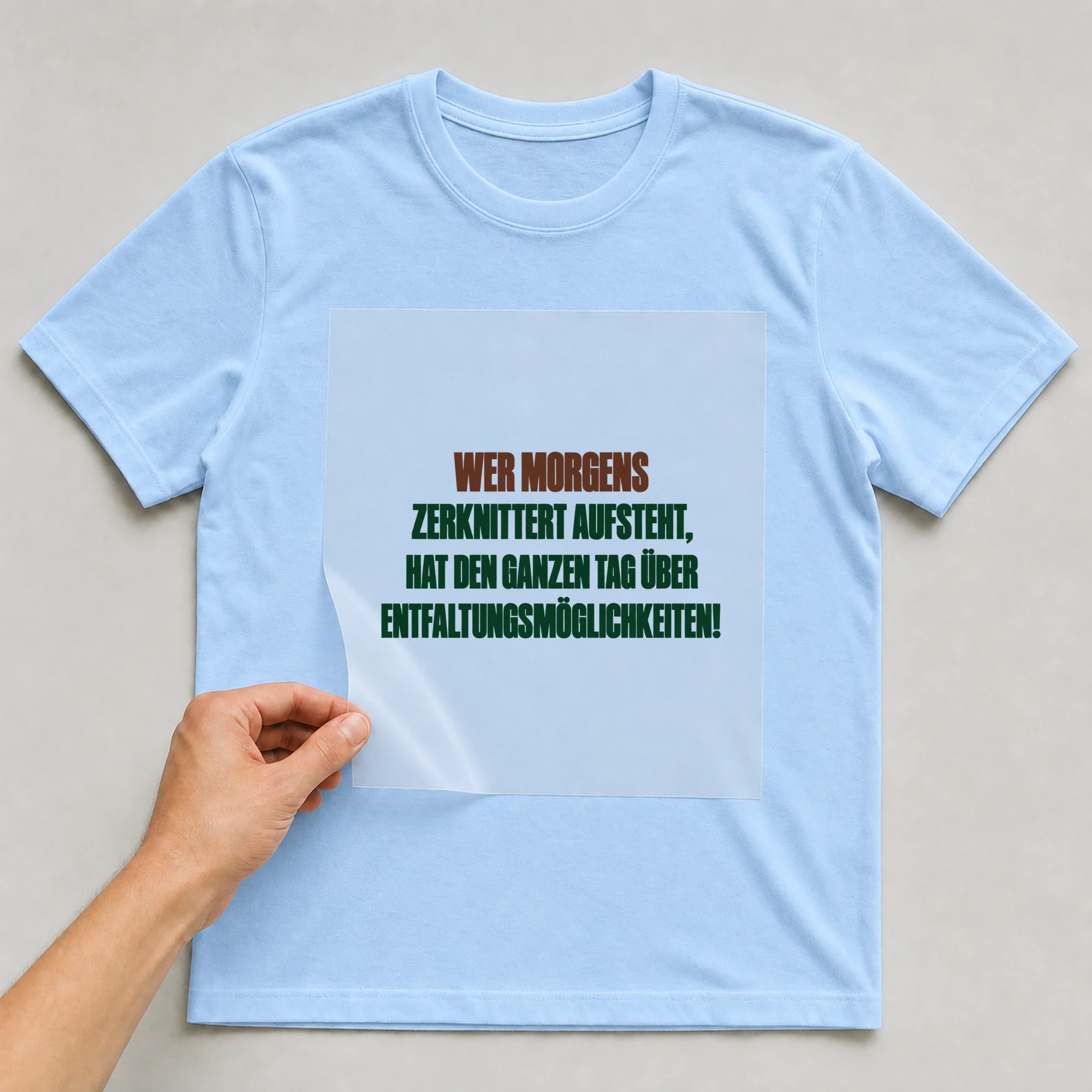 Bügelbild „WER MORGENS ZERKNITTERT AUFSTEHT, HAT DEN GANZEN TAG ÜBER ENTFALTUNGSMÖGLICHKEITEN!“ auf babyblauem T-Shirt, Folie wird aufgelegt
