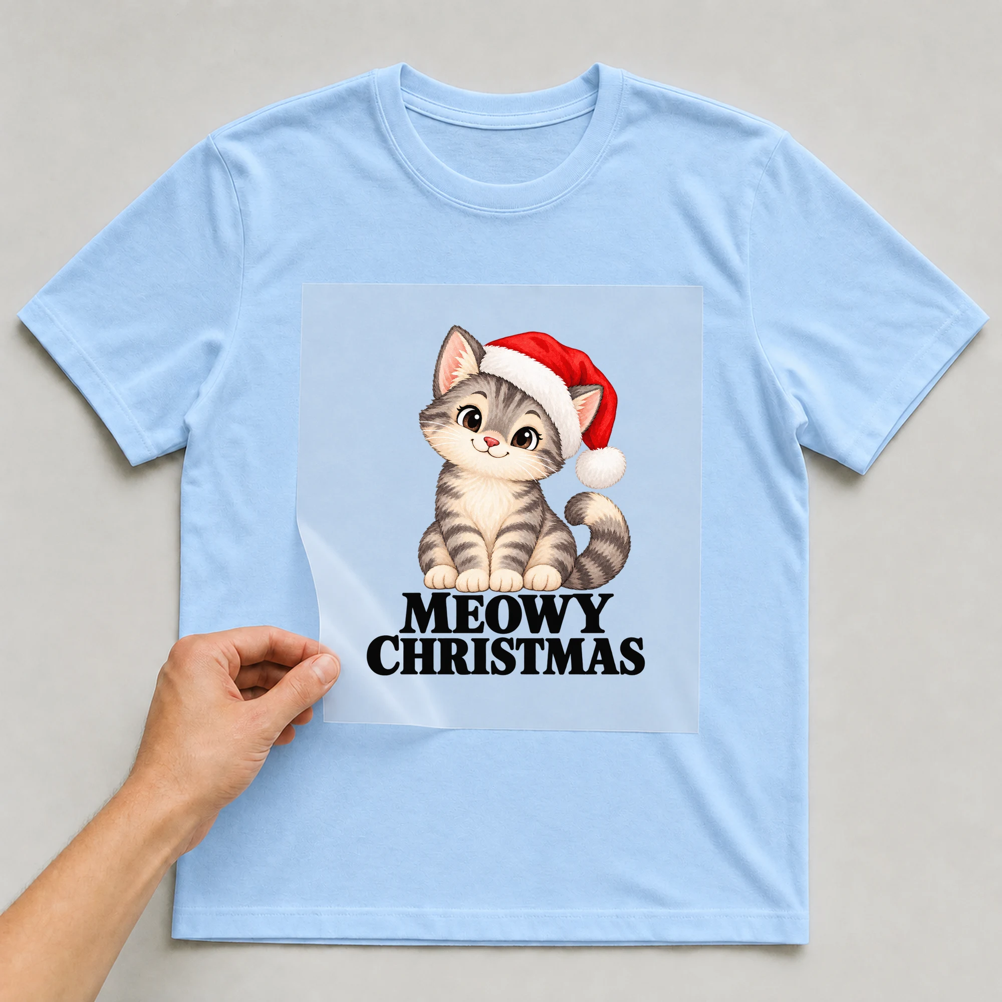 Bügelbild „Meowy Christmas“ auf babyblauem T-Shirt, Folie wird aufgelegt