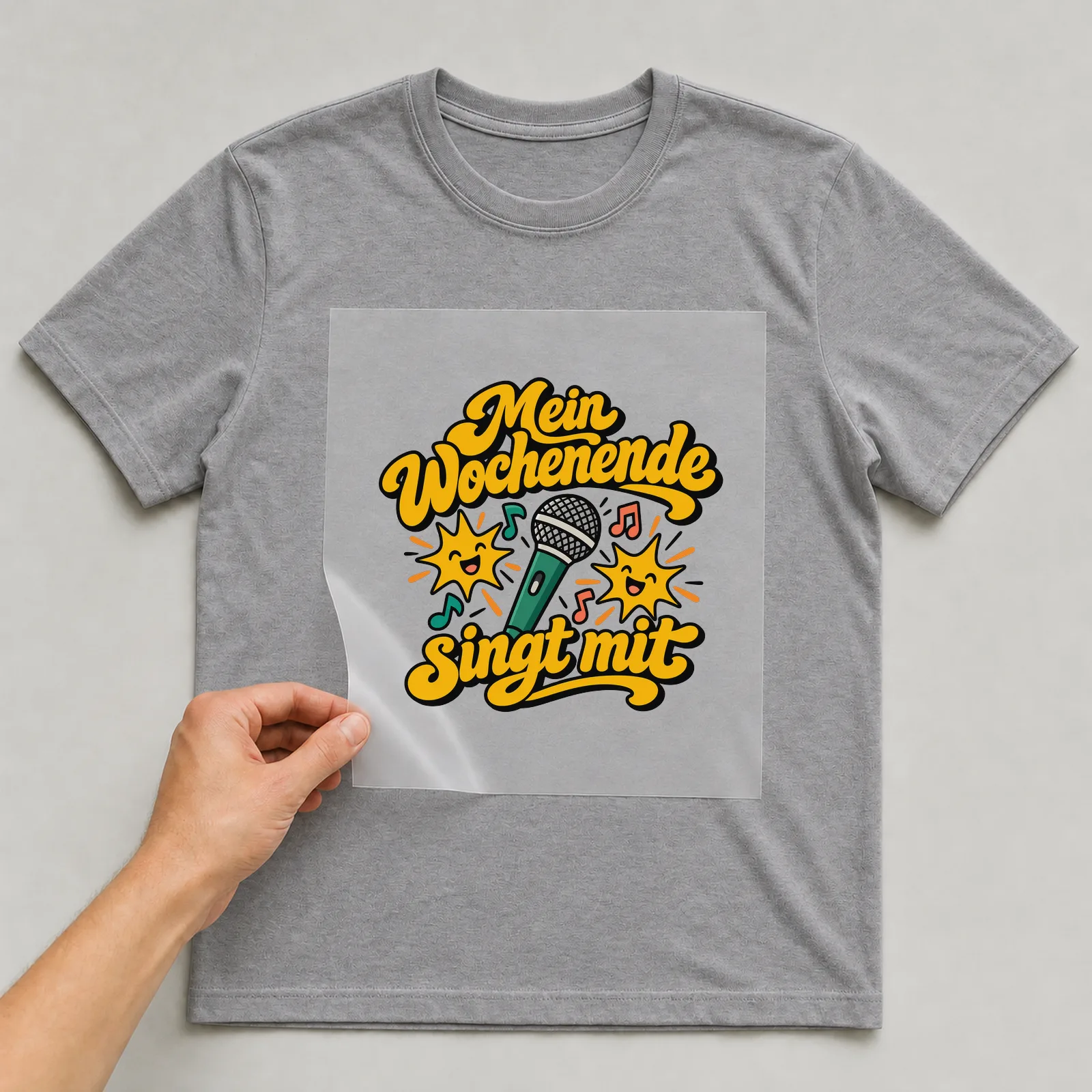 Bügelbild „Mein Wochenende singt mit“ auf grauem T-Shirt, Folie wird aufgelegt
