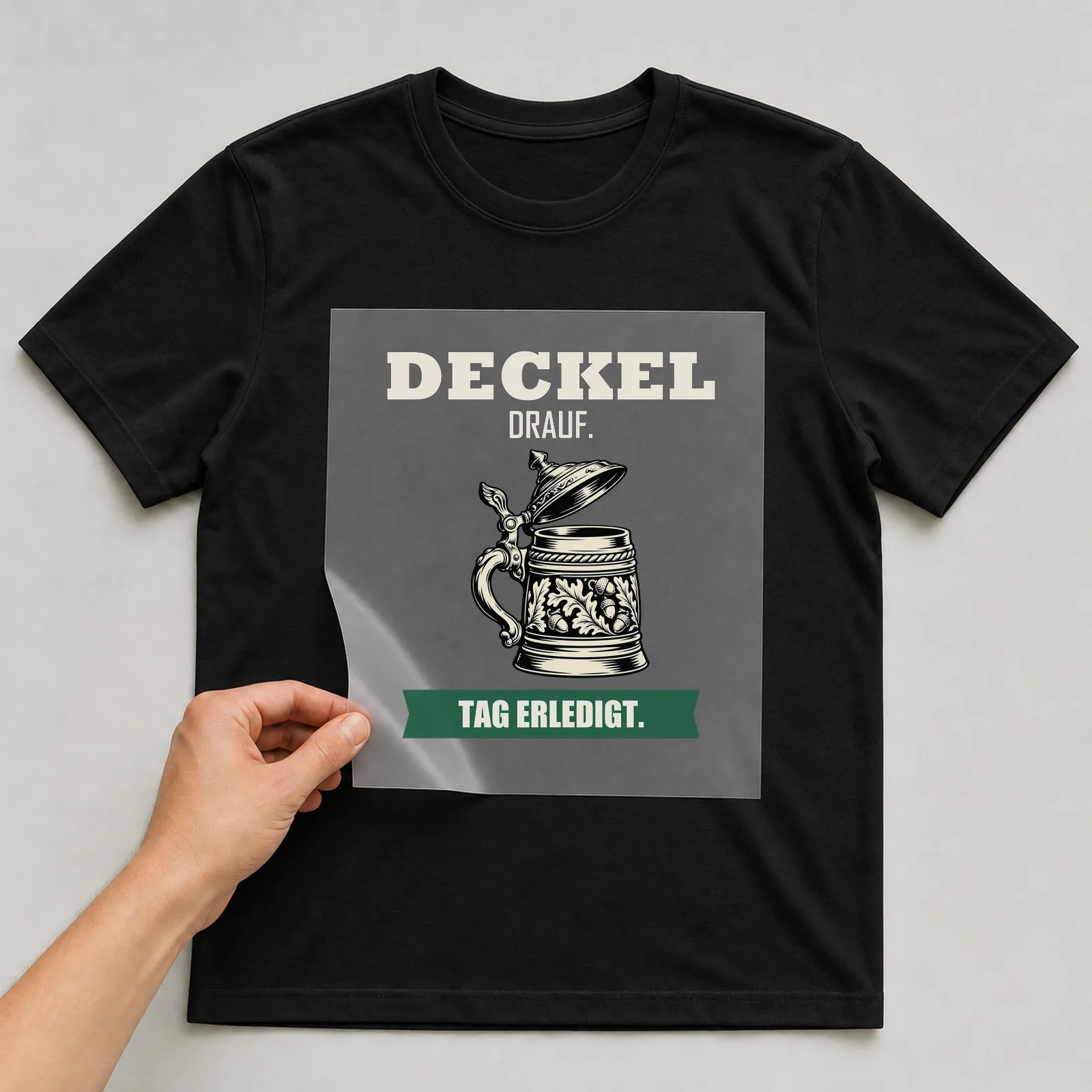 Bügelbild „Deckel drauf. Tag erledigt.“ auf schwarzem T-Shirt, Folie wird aufgelegt
