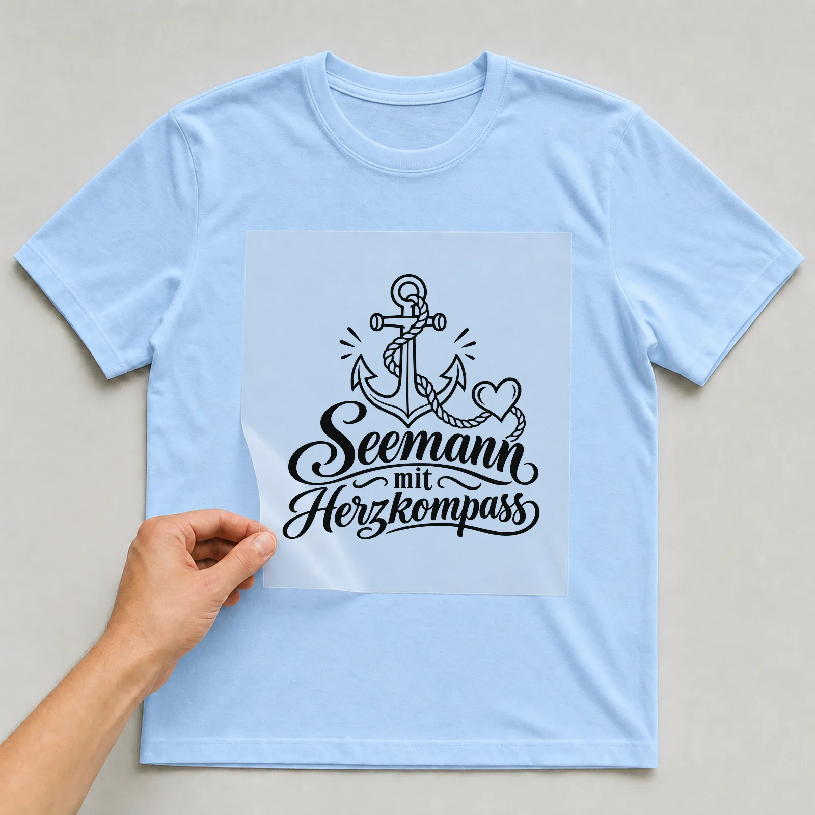 Bügelbild „Seemann mit Herzkompass“ auf hellblauem T-Shirt, Folie wird aufgelegt