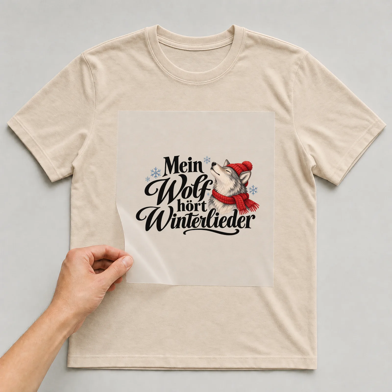 Bügelbild „Mein Wolf hört Winterlieder“ auf beigem T-Shirt, Folie wird aufgelegt