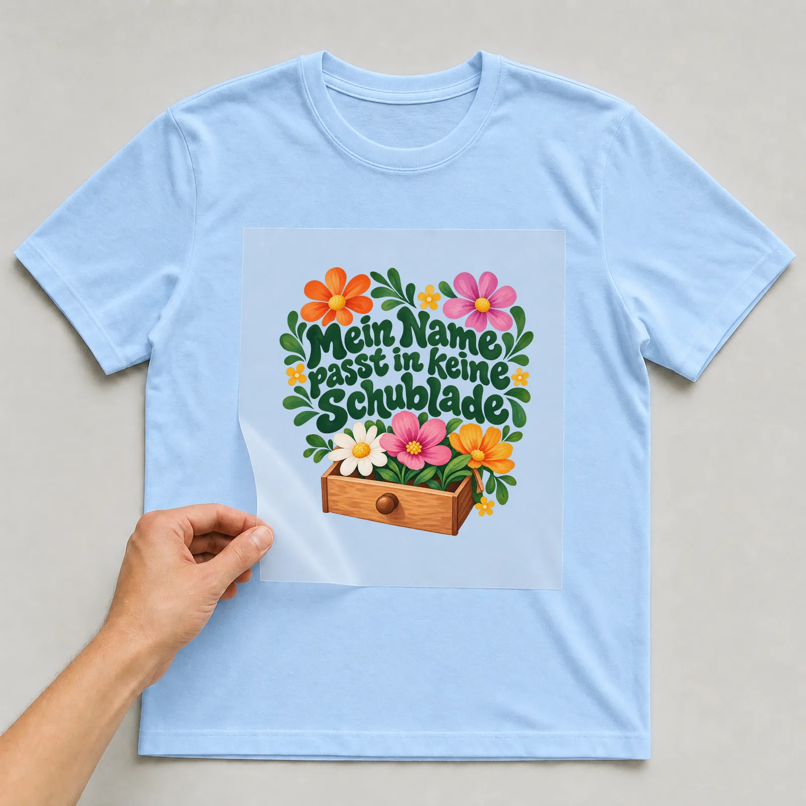 Bügelbild „Mein Name passt in keine Schublade“ auf hellblauem T-Shirt, Folie wird aufgelegt